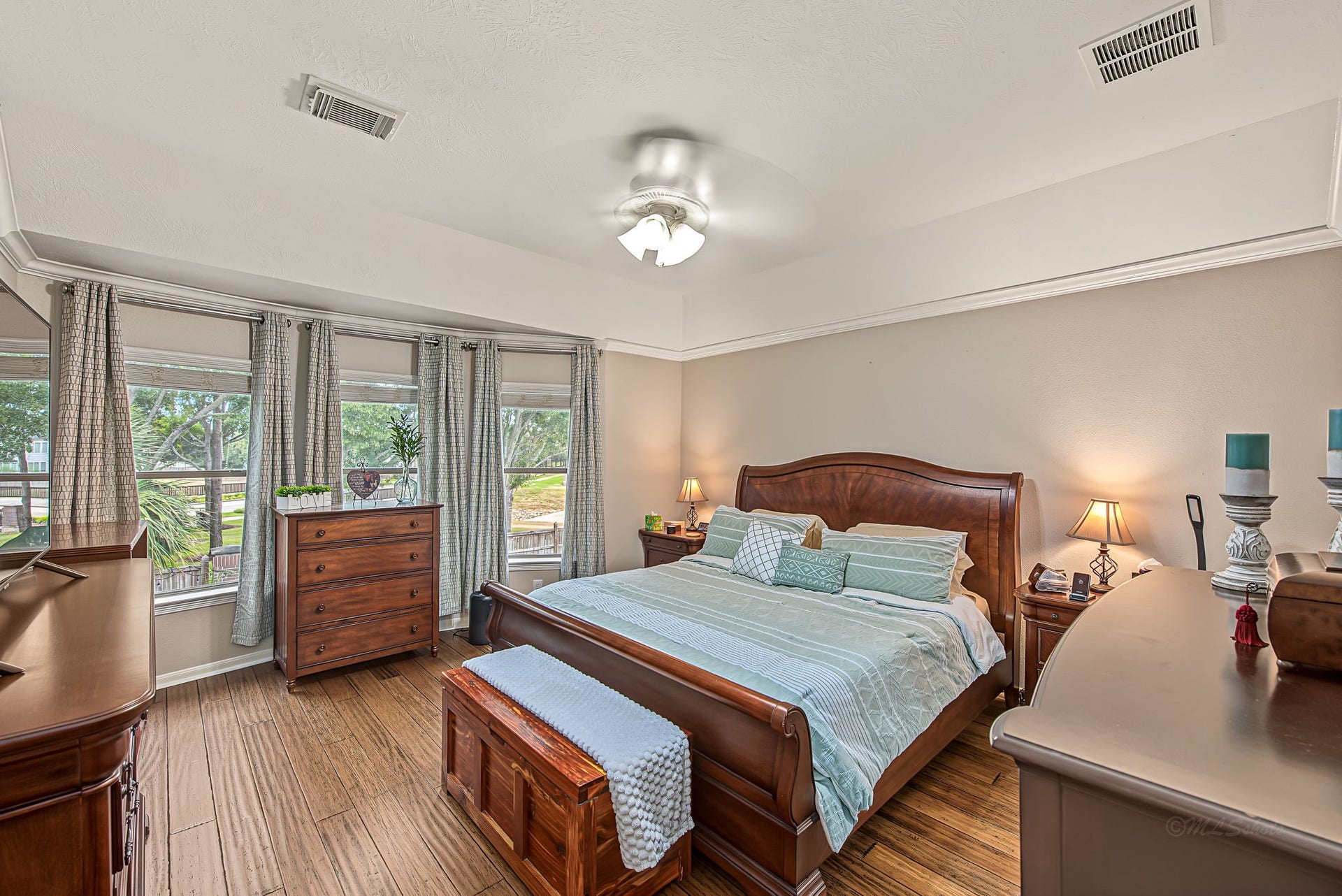 21223 Dover Park Lane, Katy, TX 77450 Spacious and inviting bedroom with warm wood flooring, featuring a large bed and elegant furnishings. Natural light pours in through multiple windows, highlighting the serene decor and creating a cozy retreat.