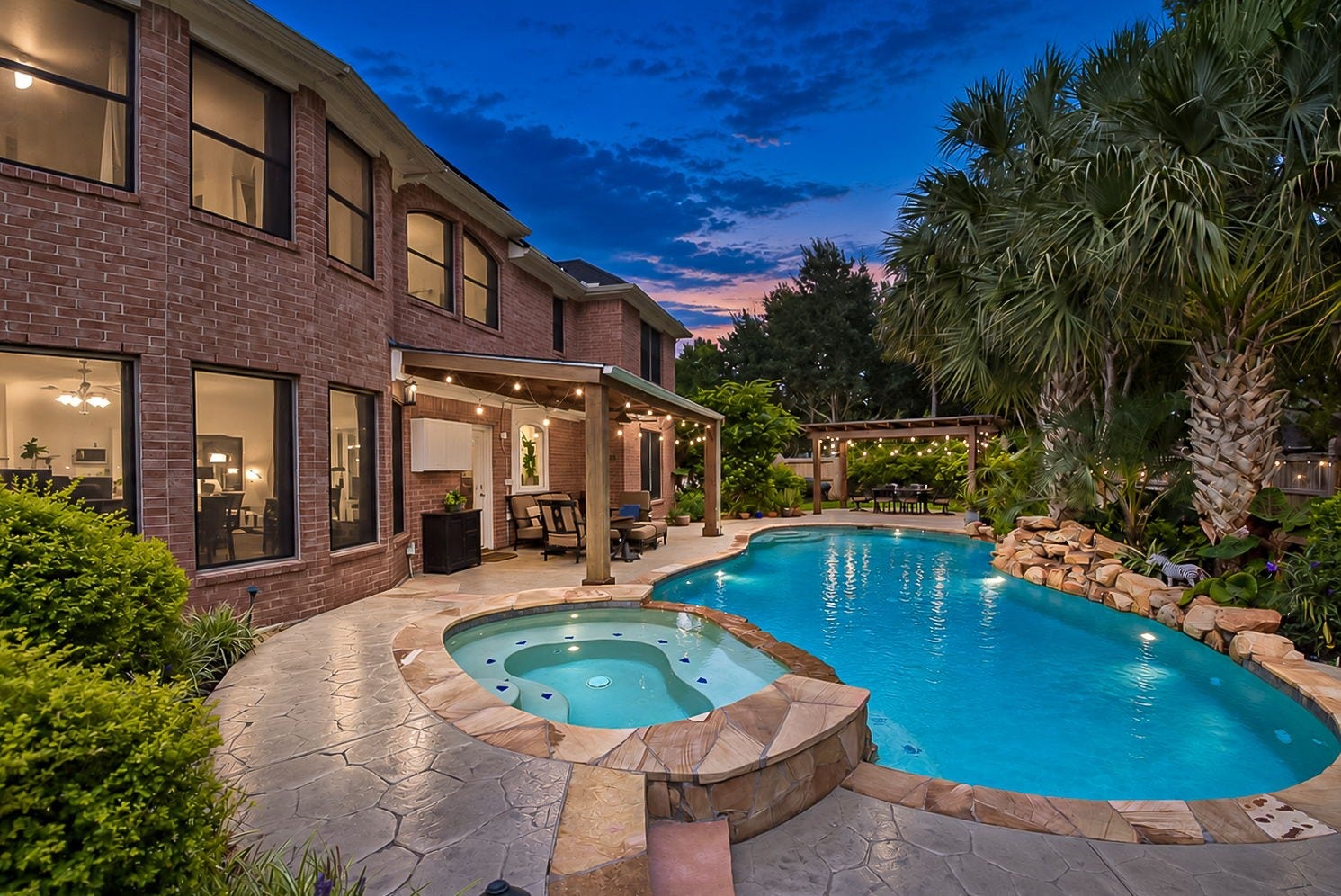 21223 Dover Park Lane, Katy, TX 77450 Stunning backyard oasis featuring a sparkling pool with waterfall, attached spa, and charming covered patio, perfect for entertaining and relaxation amidst lush landscaping.