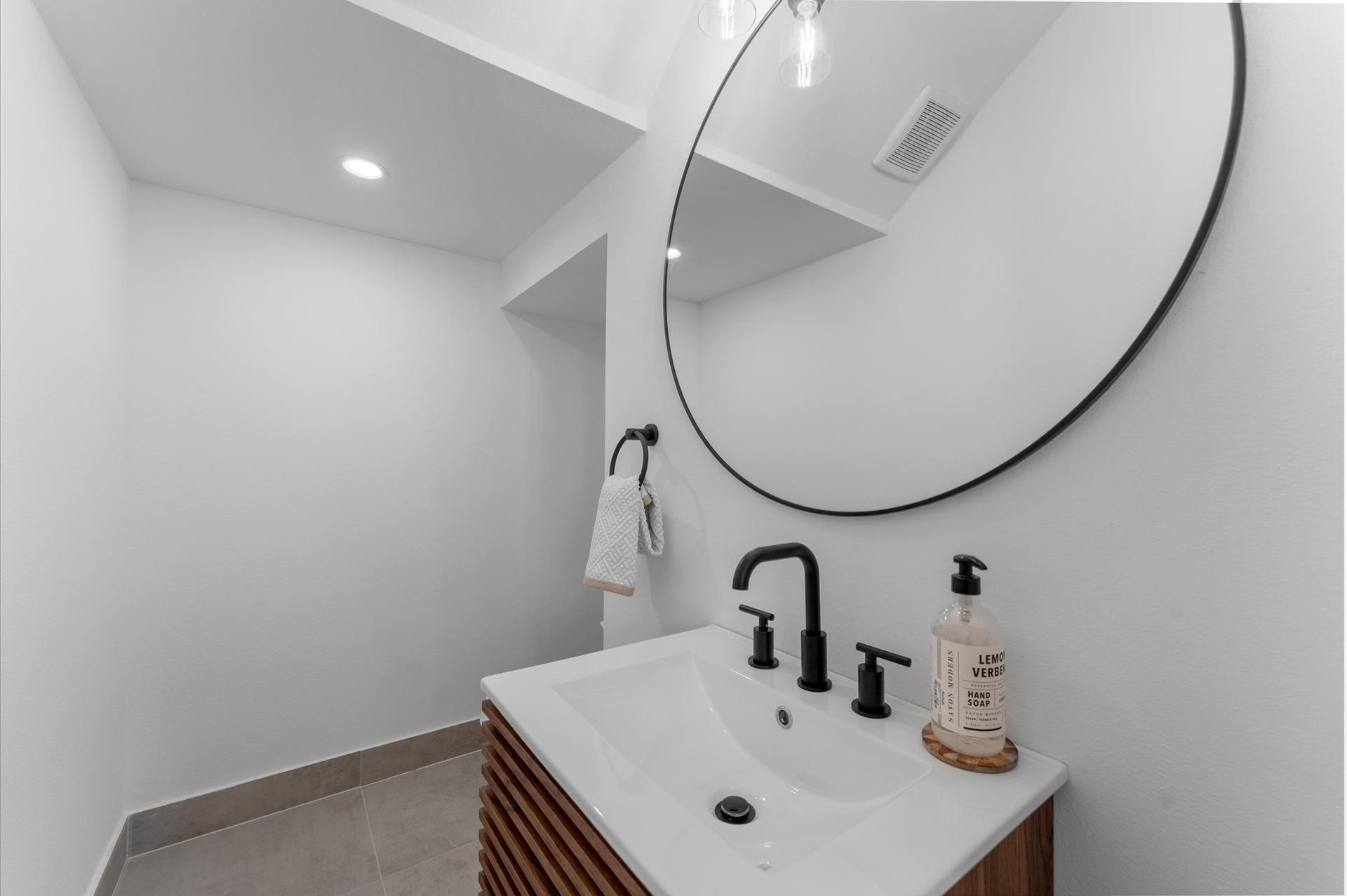 1009 Tuskegee Heights Lane, Houston, TX 77091 This stylish second-floor powder room blends modern elegance with functional design. Featuring contemporary finishes throughout, the space includes a sleek vanity with clean lines and minimalist hardware. The vanity is paired with a statement mirror and bold lighting fixtures that add visual interest.