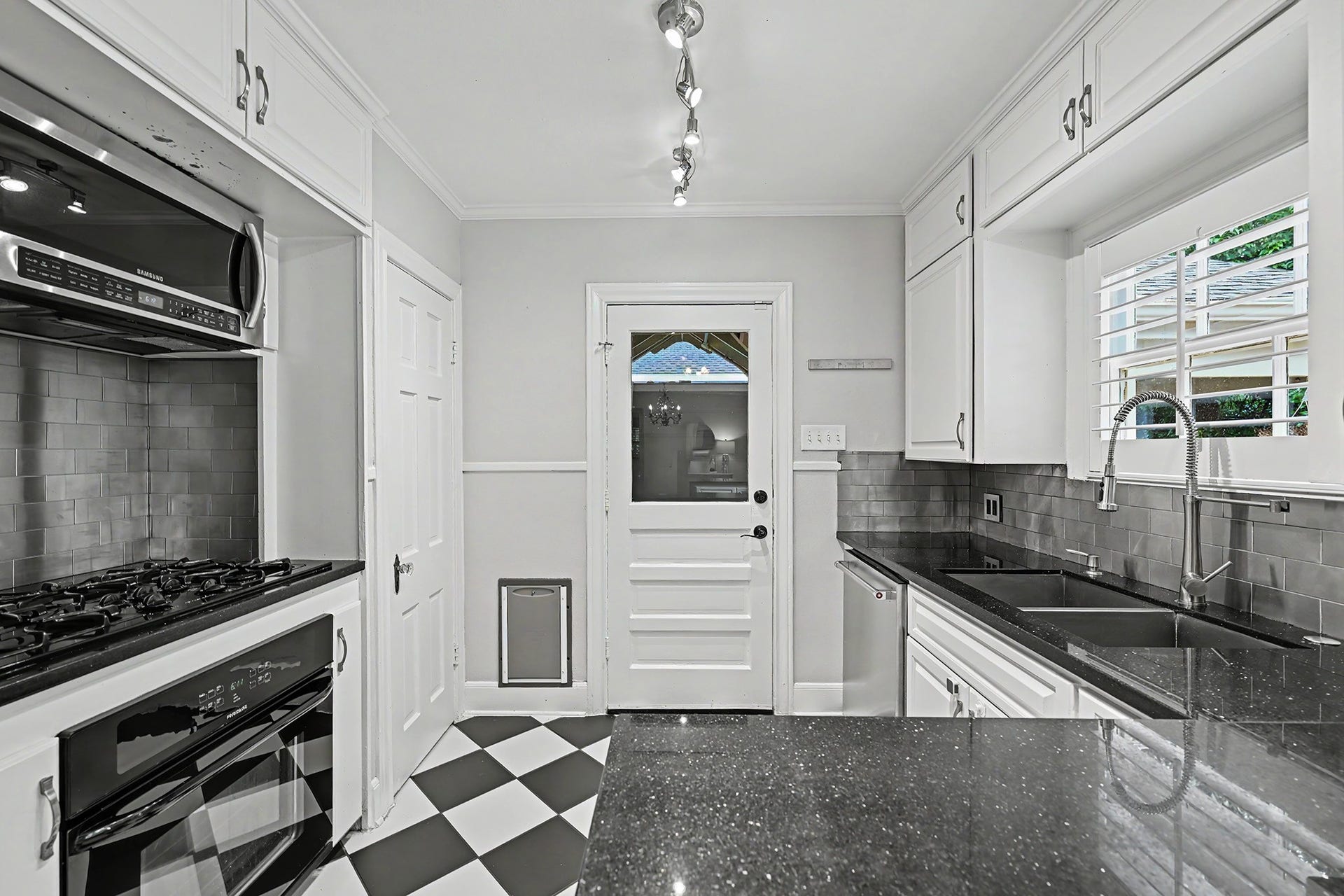 320 W 33rd Street, Houston, TX 77018 Classic black-and-white tile flooring pairs with a modern backsplash and updated appliances, including a gas cooktop and large sink. Back door leads to the covered deck with fan and porch swing.