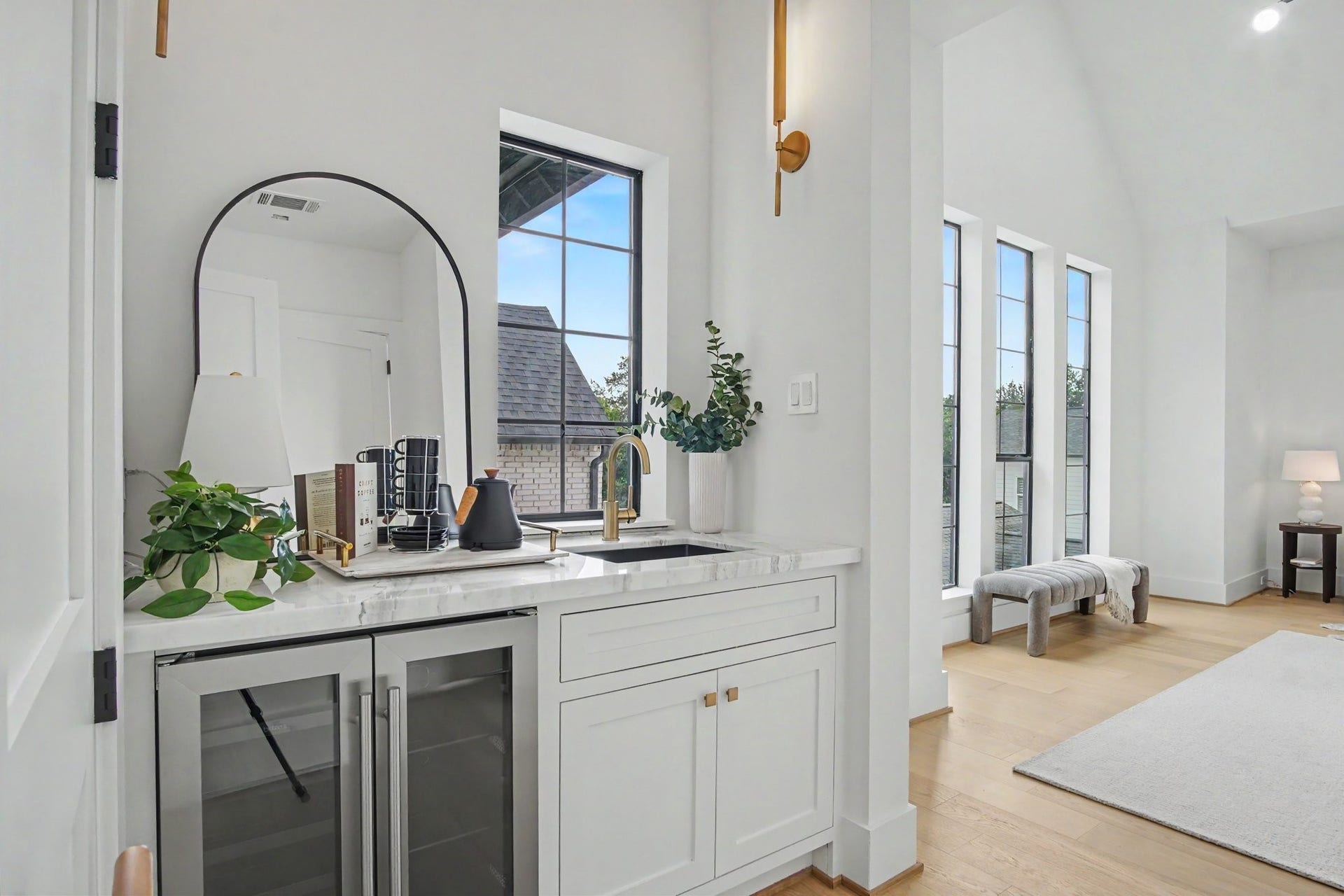 705 Walton Street, Houston, TX 77009 Stylish wet bar with sleek cabinetry and a marble countertop, complemented by elegant fixtures, seamlessly flows into a bright, airy room with expansive windows and warm hardwood floors.