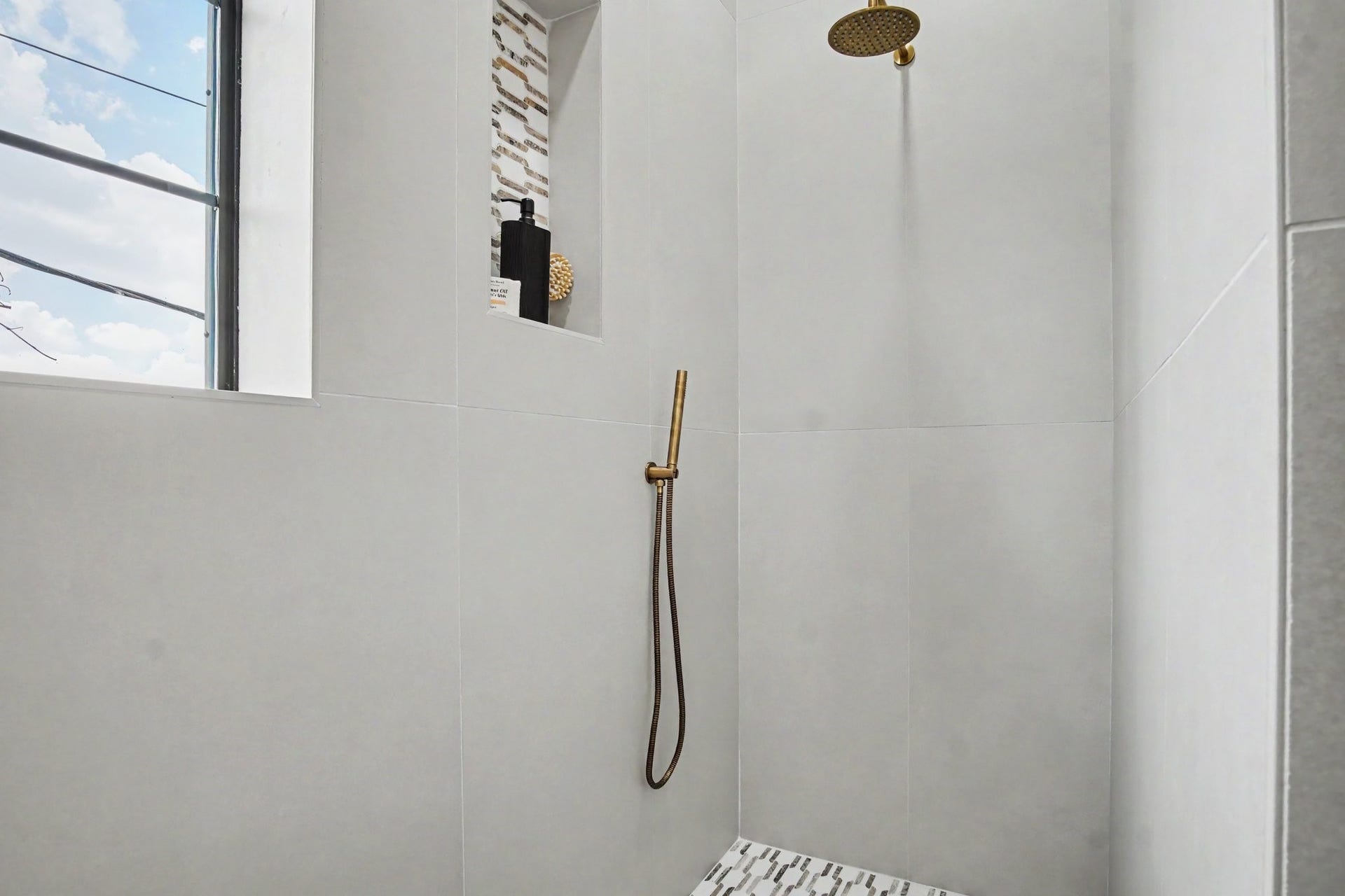 705 Walton Street, Houston, TX 77009 Elegant shower space featuring modern fixtures, a sleek rain showerhead, and built-in shelving, highlighted by natural light from a nearby window.