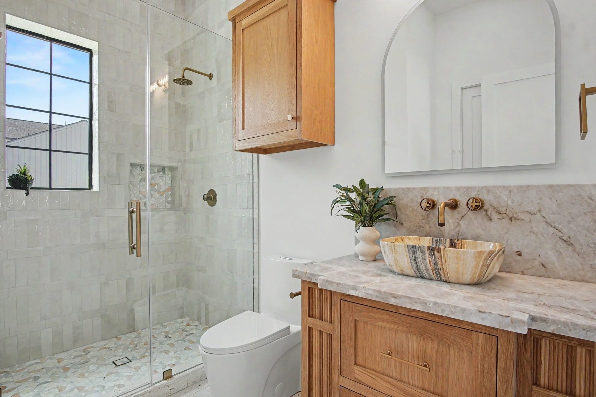 705 Walton Street, Houston, TX 77009 Elegant bathroom featuring a glass-enclosed shower with mosaic tile accents, a modern stone vessel sink on a quartzite countertop, and sleek wooden cabinetry for a warm touch.