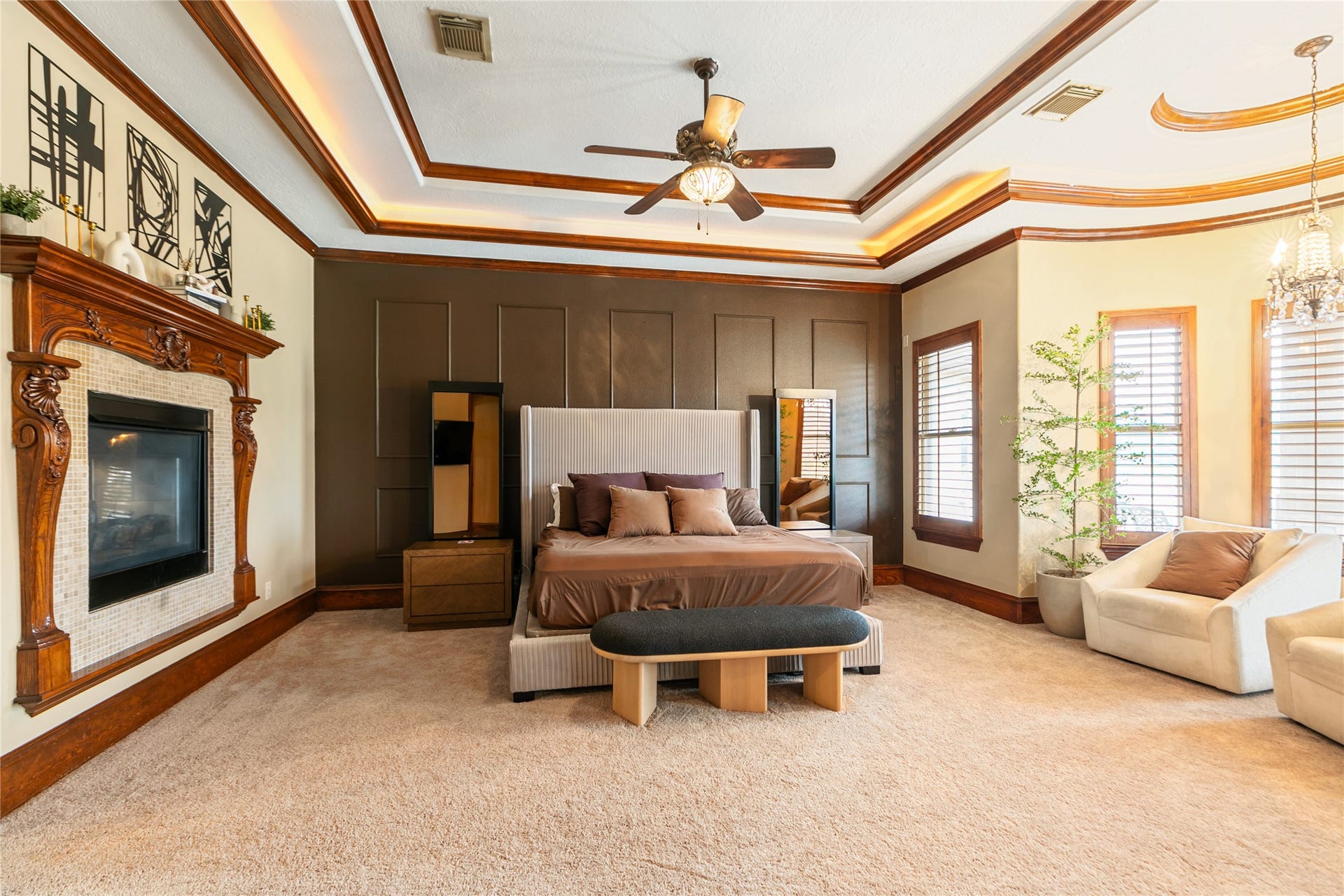 The luxurious primary bedroom, highlighted by the fireplace, large windows, beautiful paneling, molding, and an elegant tray ceiling, creates a warm and inviting retreat for relaxation.