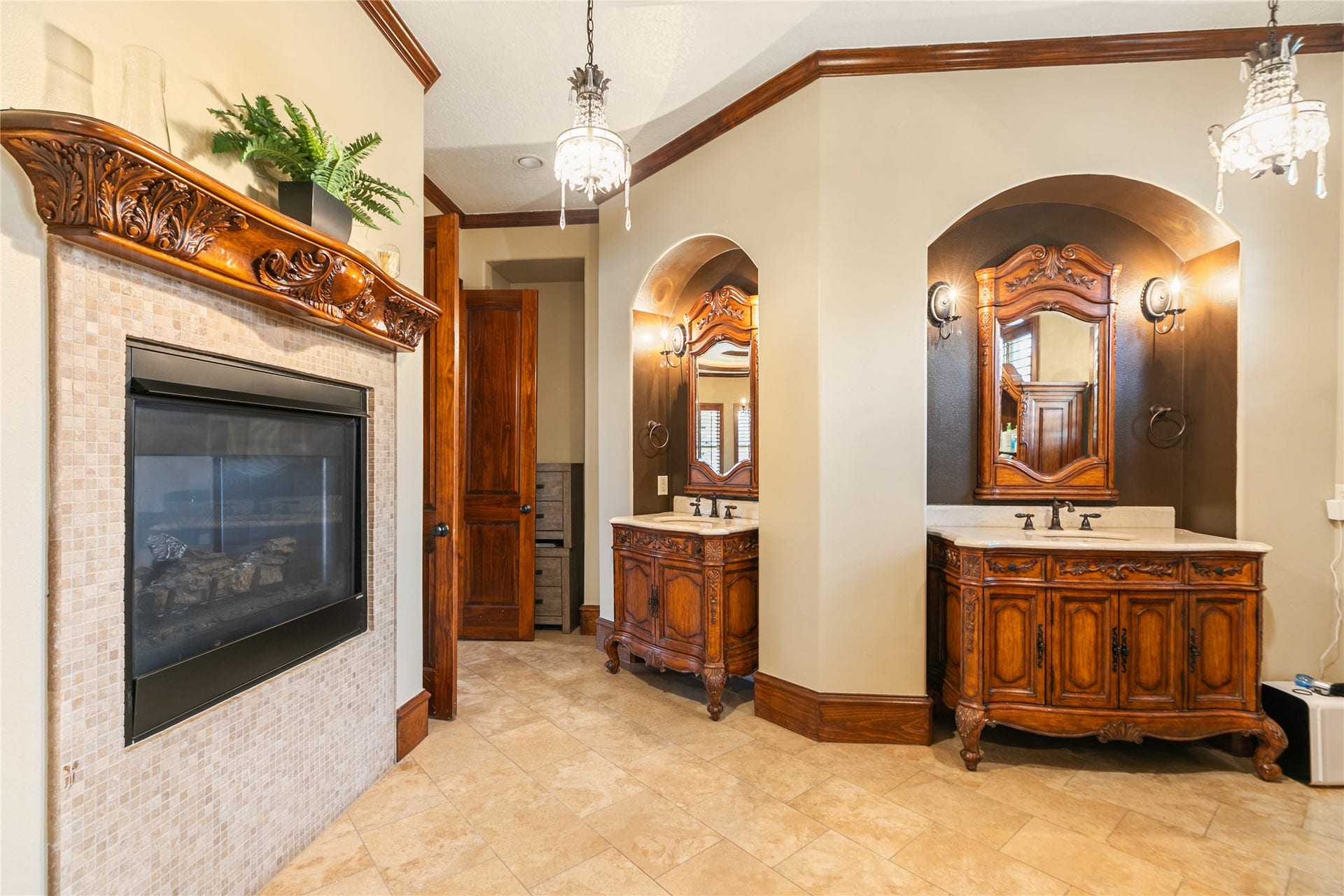 The primary bath features rich wood vanities set within attractive alcoves and a dual-sided fireplace, creating a warm and inviting retreat.