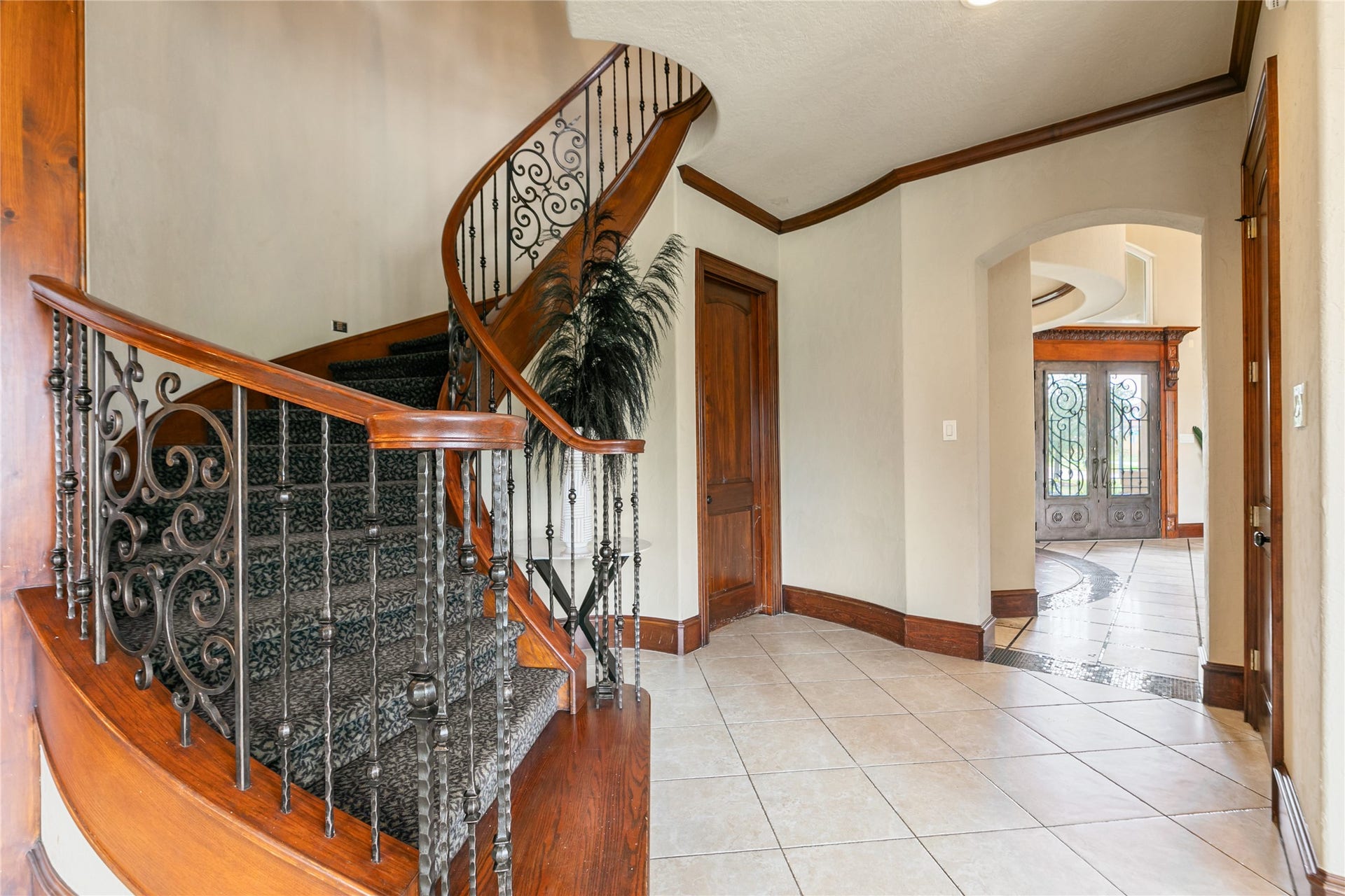 View from the base of the stunning curved staircase with walkway to the double front doors, showcasing the homes exquisite iron detailing.