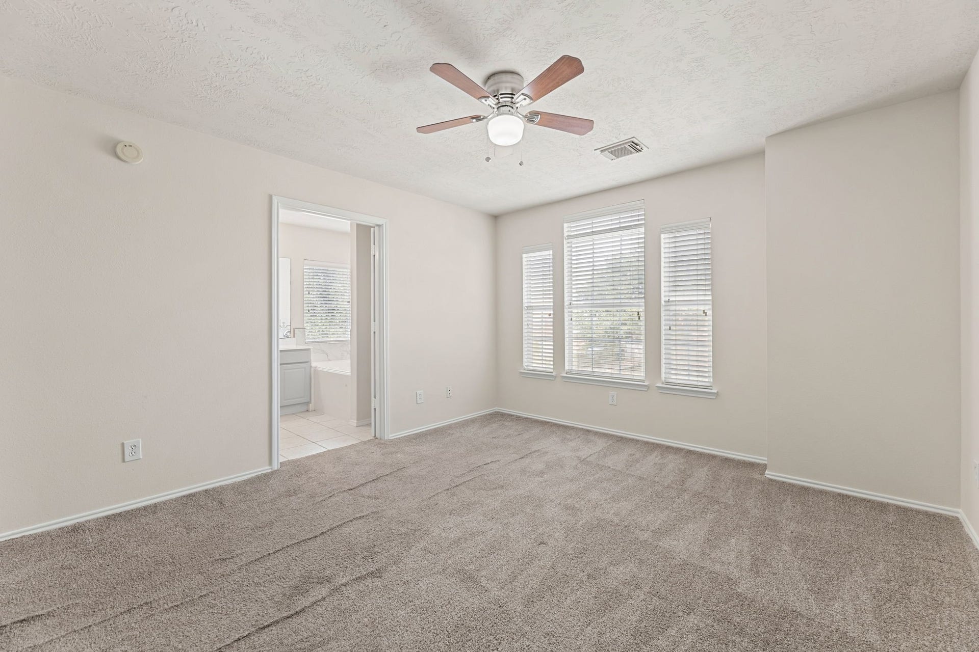 Primary bedroom comes with plush carpet, a ceiling fan, and a private entry to the ensuite bath.