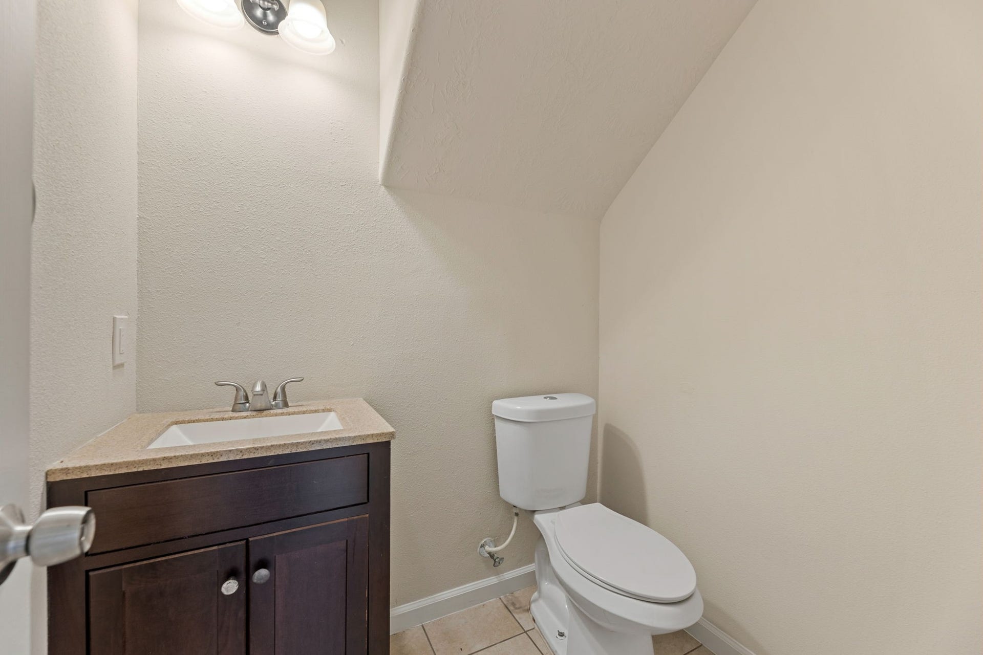 A downstairs half bath with a dark wood vanity and a speckled countertop, tucked neatly under the stairs.