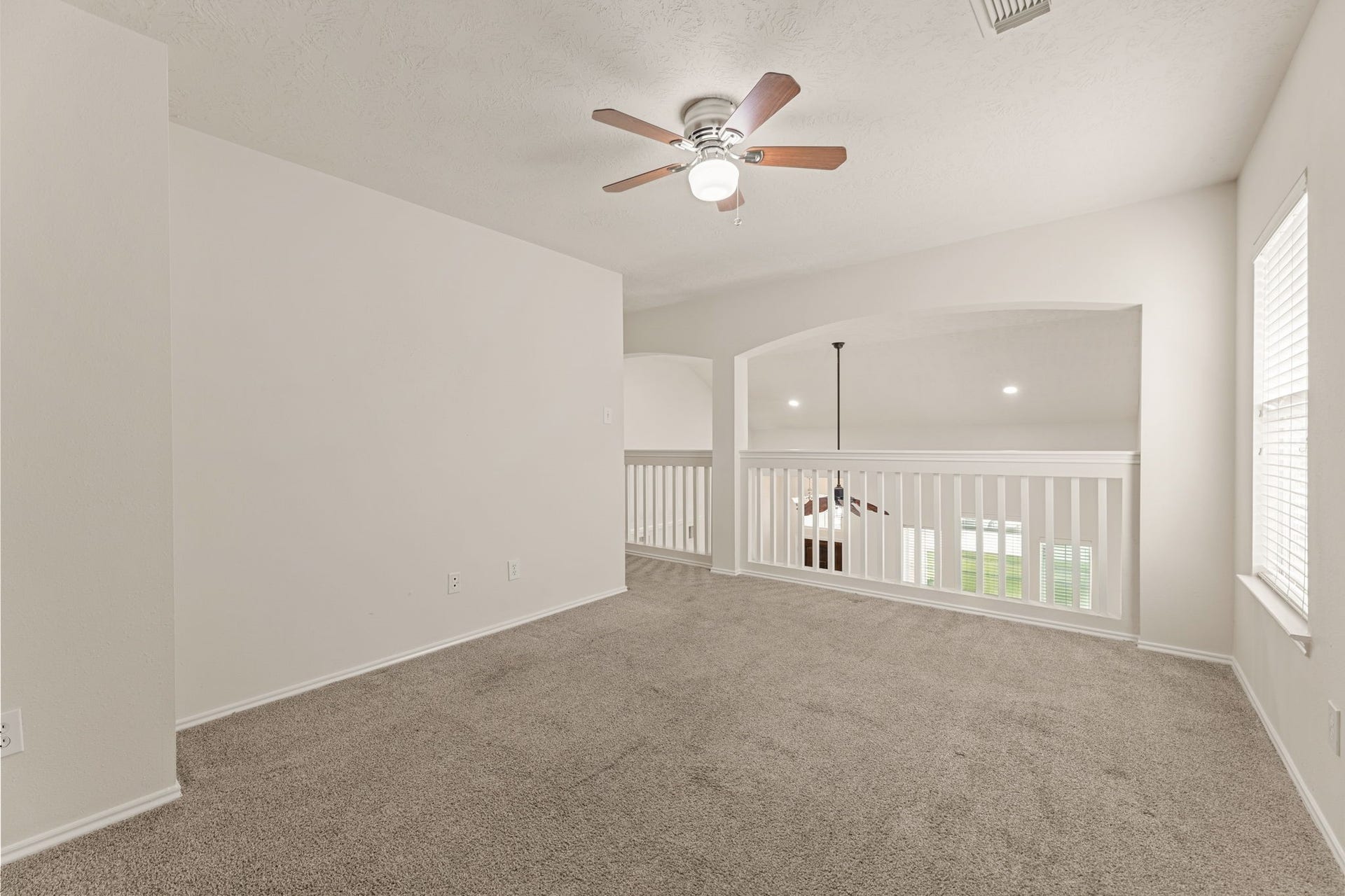 An open loft with a window and a railed balcony that looks down on the formal living area below.