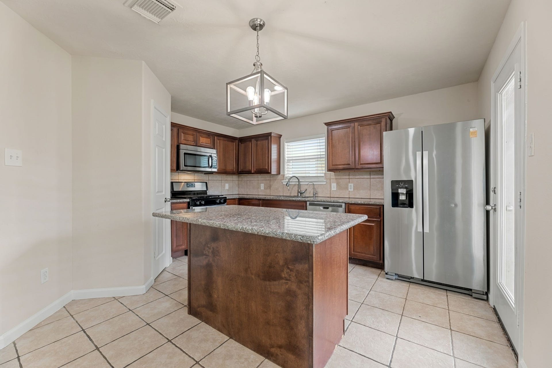 Warm wood cabinetry, granite counters, a tile backsplash, and a full suite of stainless steel appliances.