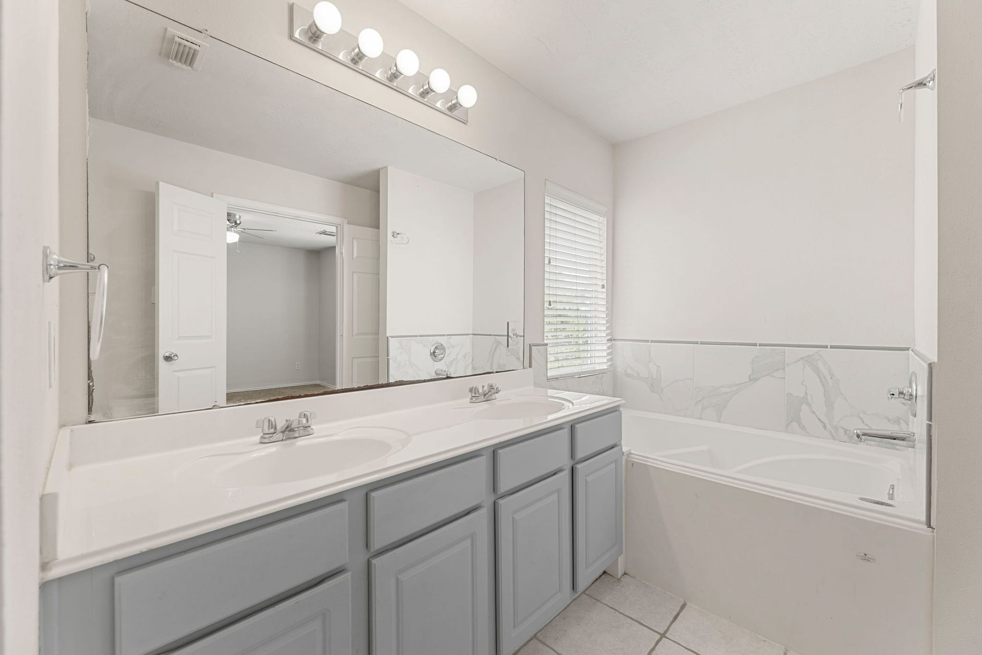 Dual sinks sit next to a garden tub framed in marble-look tile, with a window for natural light.