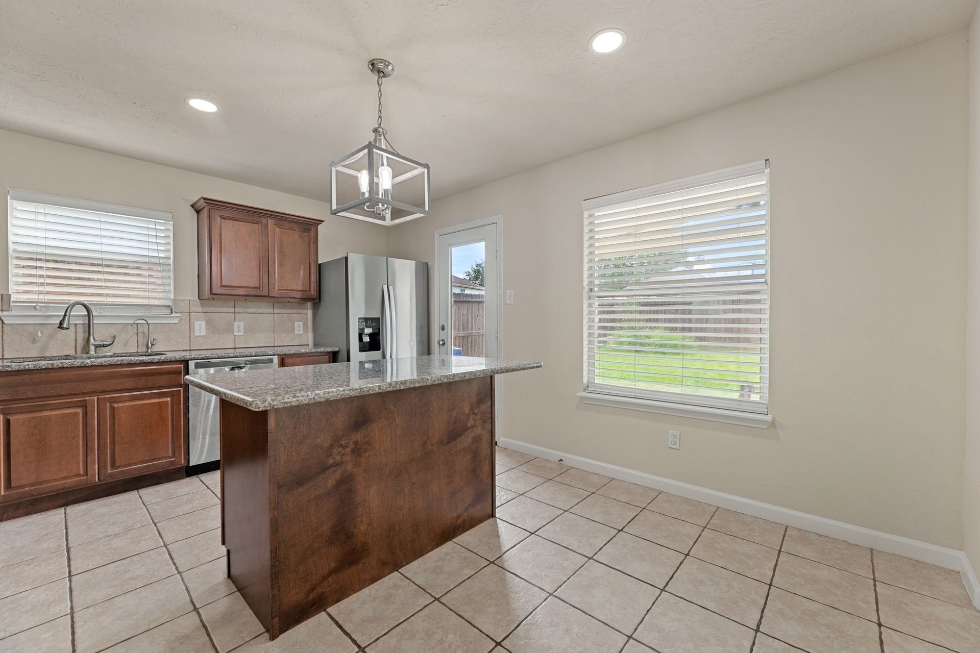 A granite-topped island with a rich wood base sits under a modern cage pendant, next to a sunny breakfast nook.