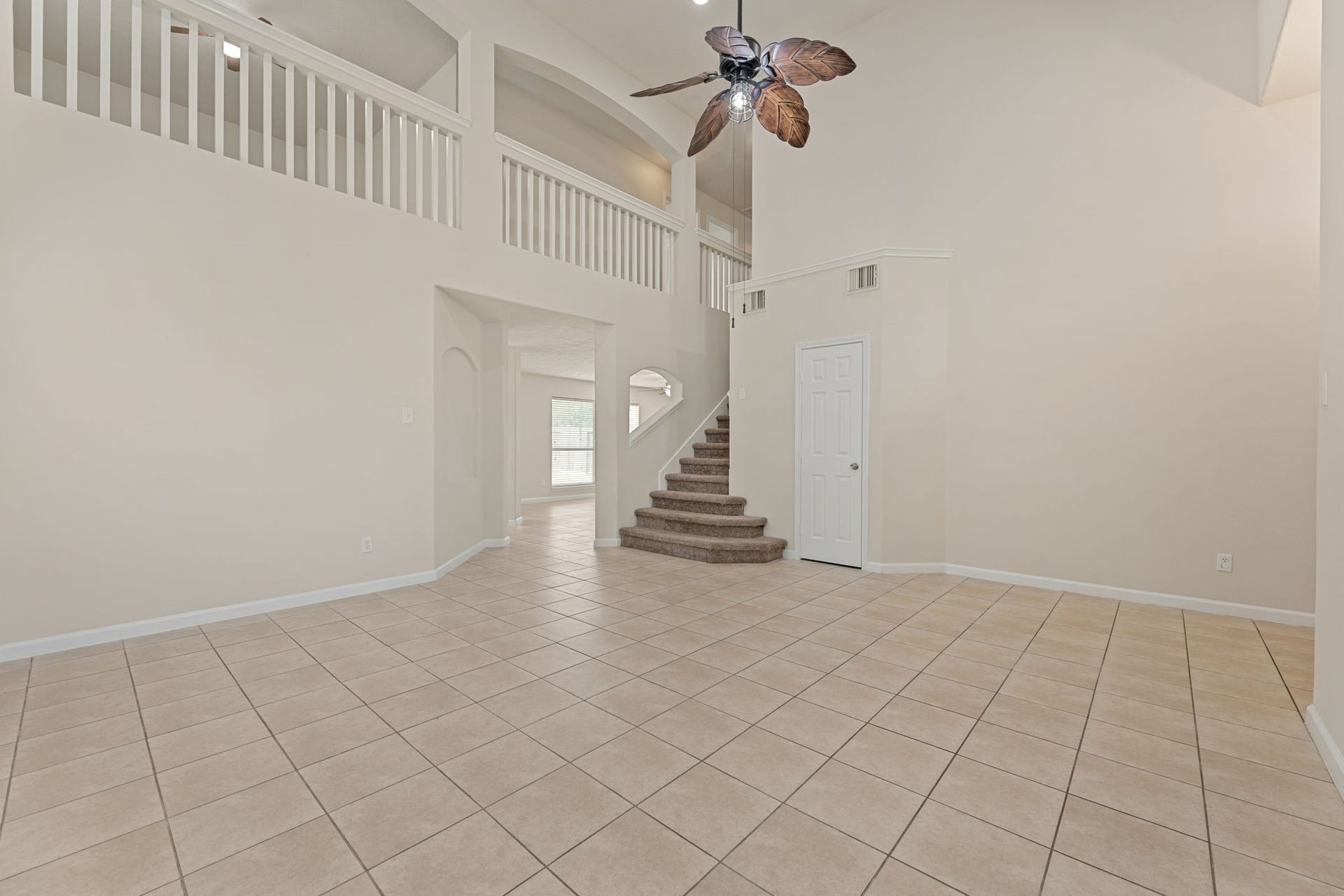 Plant ledges, a statement ceiling fan, and a carpeted staircase lead up to the second floor.