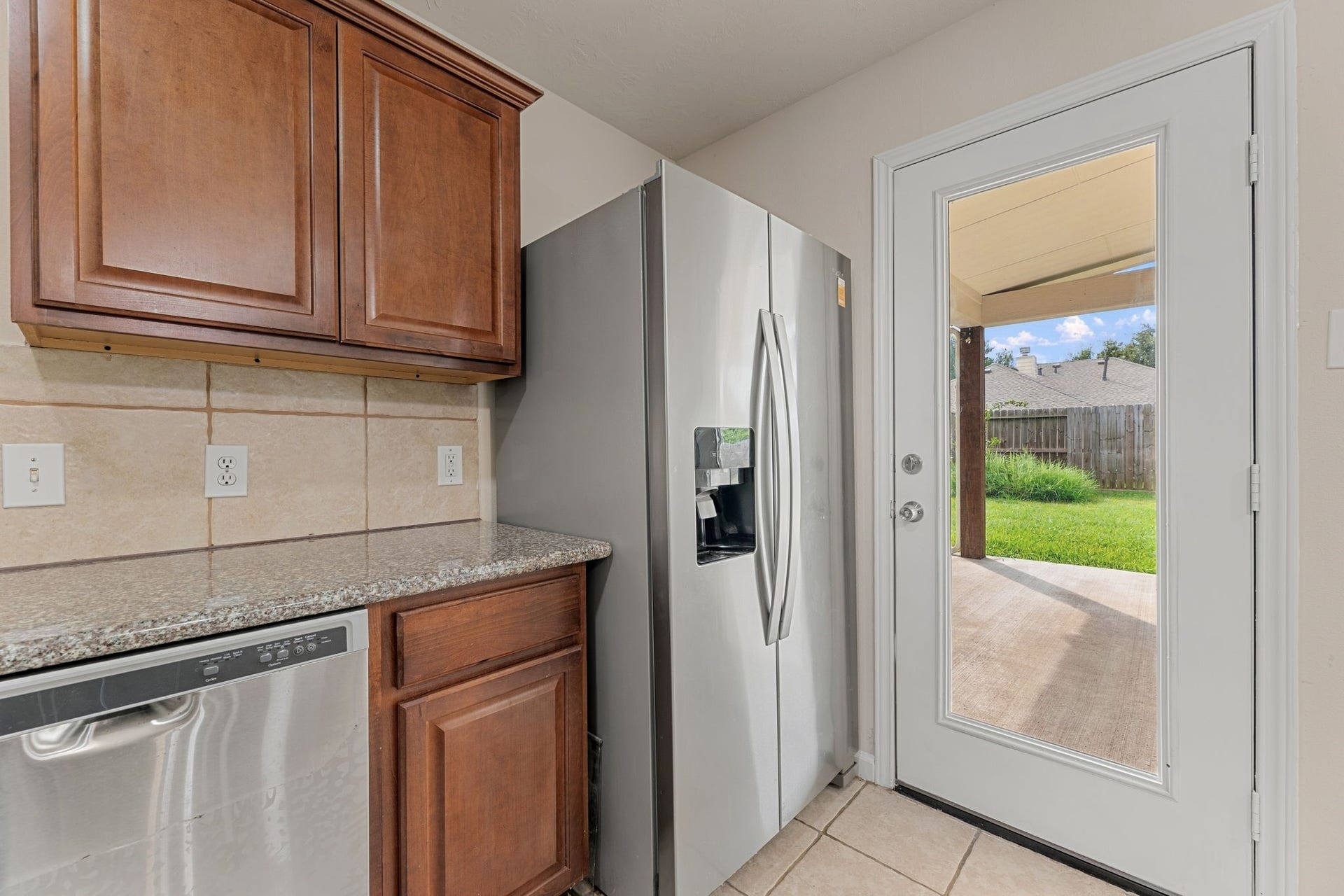 A side-by-side refrigerator with water and ice dispenser sits next to a glass door that opens onto the covered back patio.