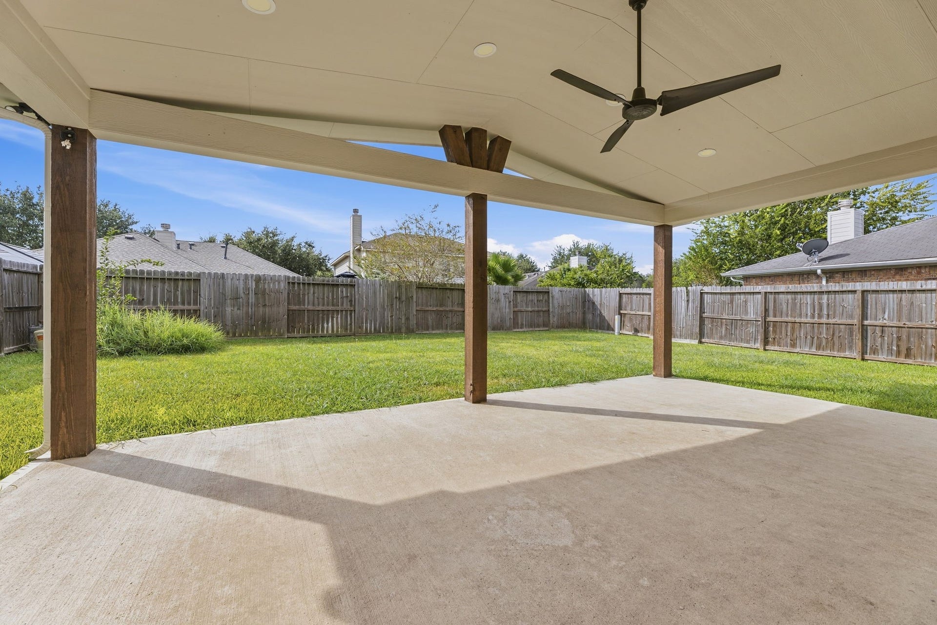 An extended patio with cedar-wrapped posts, recessed lighting, and a ceiling fan, great for Texas evenings.