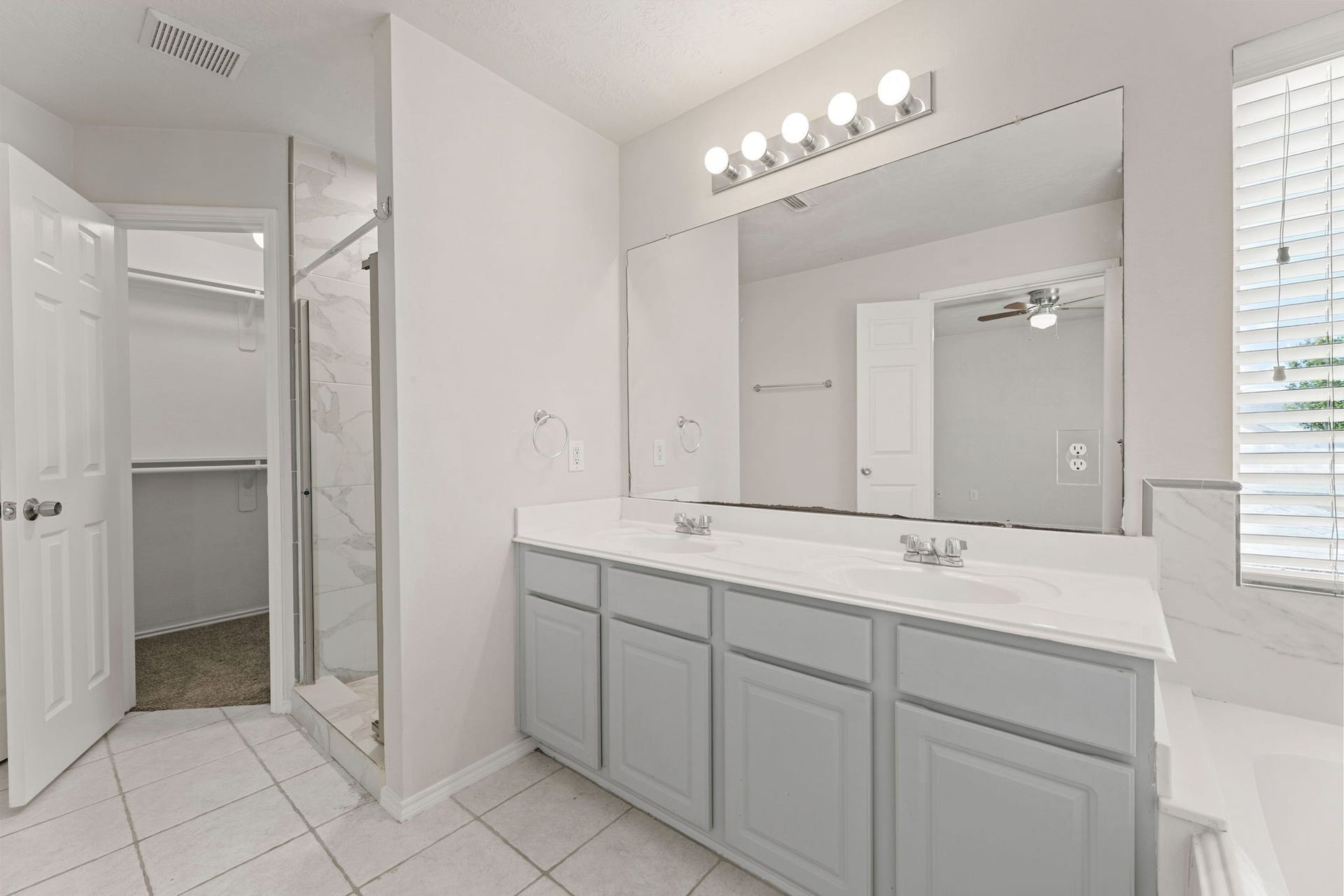 Refreshed gray cabinetry, a double vanity, a large mirror, and a walk-in shower with direct access to the closet.