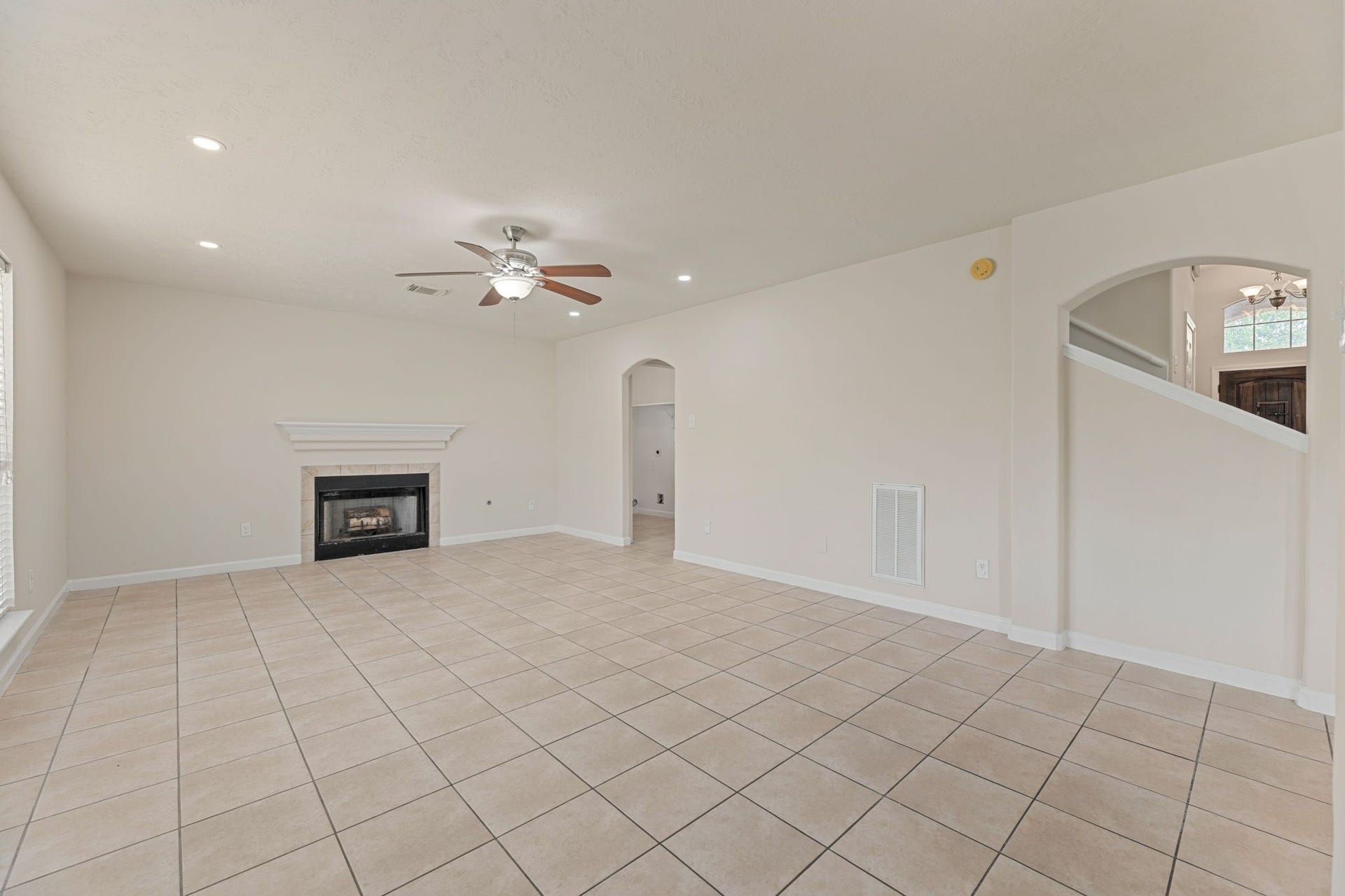 The spacious main living area has a tile-surround fireplace, a white mantel, recessed lighting, and a large window facing the backyard.
