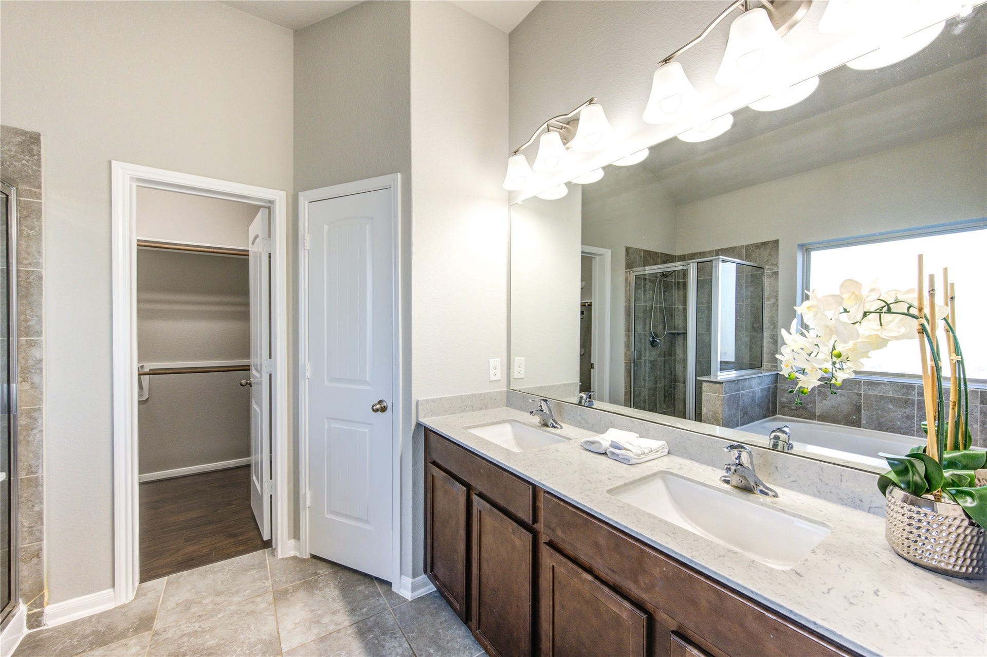 5314 Silver Ledge Drive, Katy, TX 77493 This is a modern bathroom with a double vanity featuring dark wood cabinets and a light countertop. It includes a spacious bathtub with tiled surround and large window. The room has a neutral color palette and leads into a room with hardwood flooring.