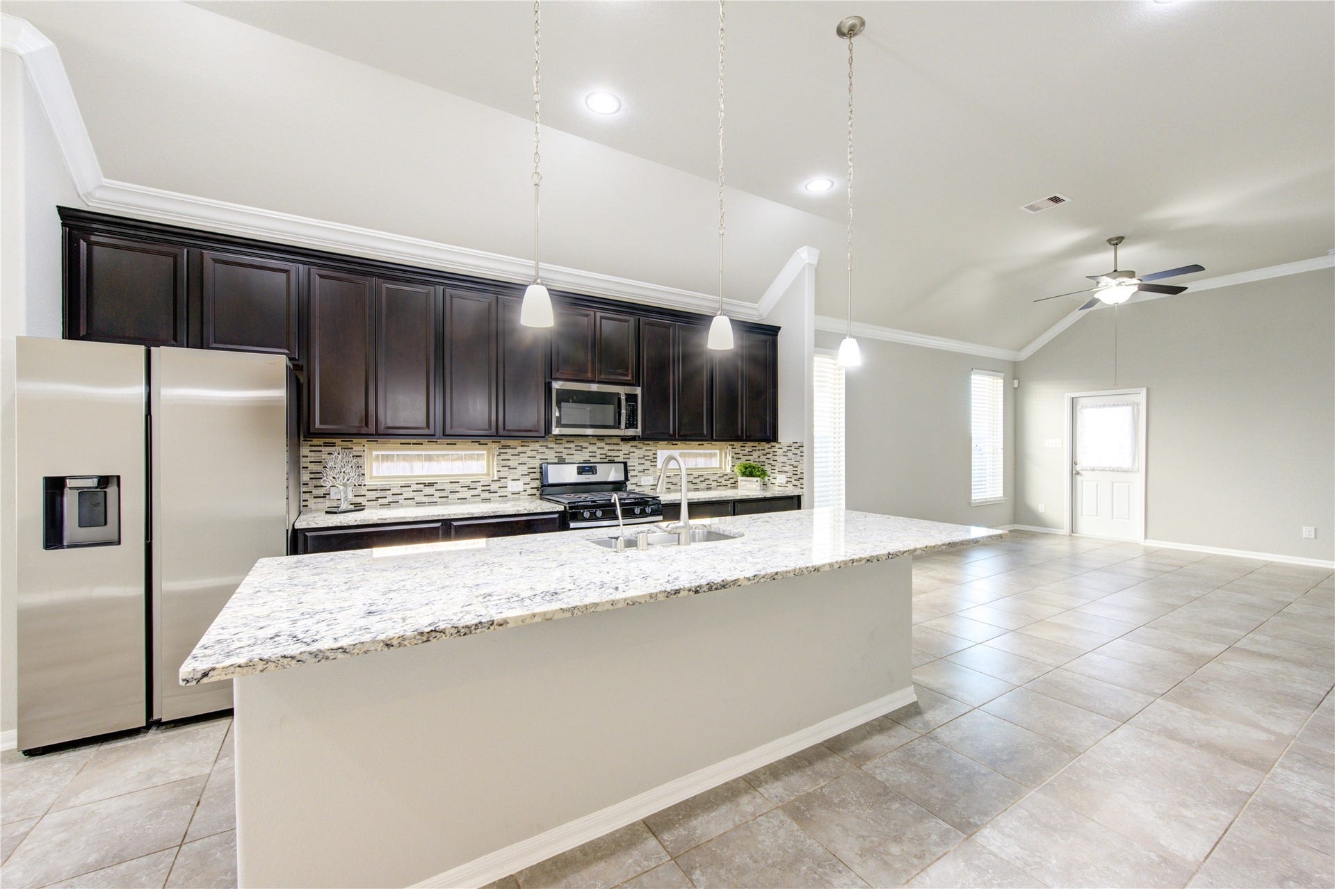 5314 Silver Ledge Drive, Katy, TX 77493 This bright, airy kitchen features large tile flooring, ample natural light from two windows, and a stylish dark wood front door with decorative glass. The space includes a modern stainless steel refrigerator and is accented by crown molding and neutral wall colors.