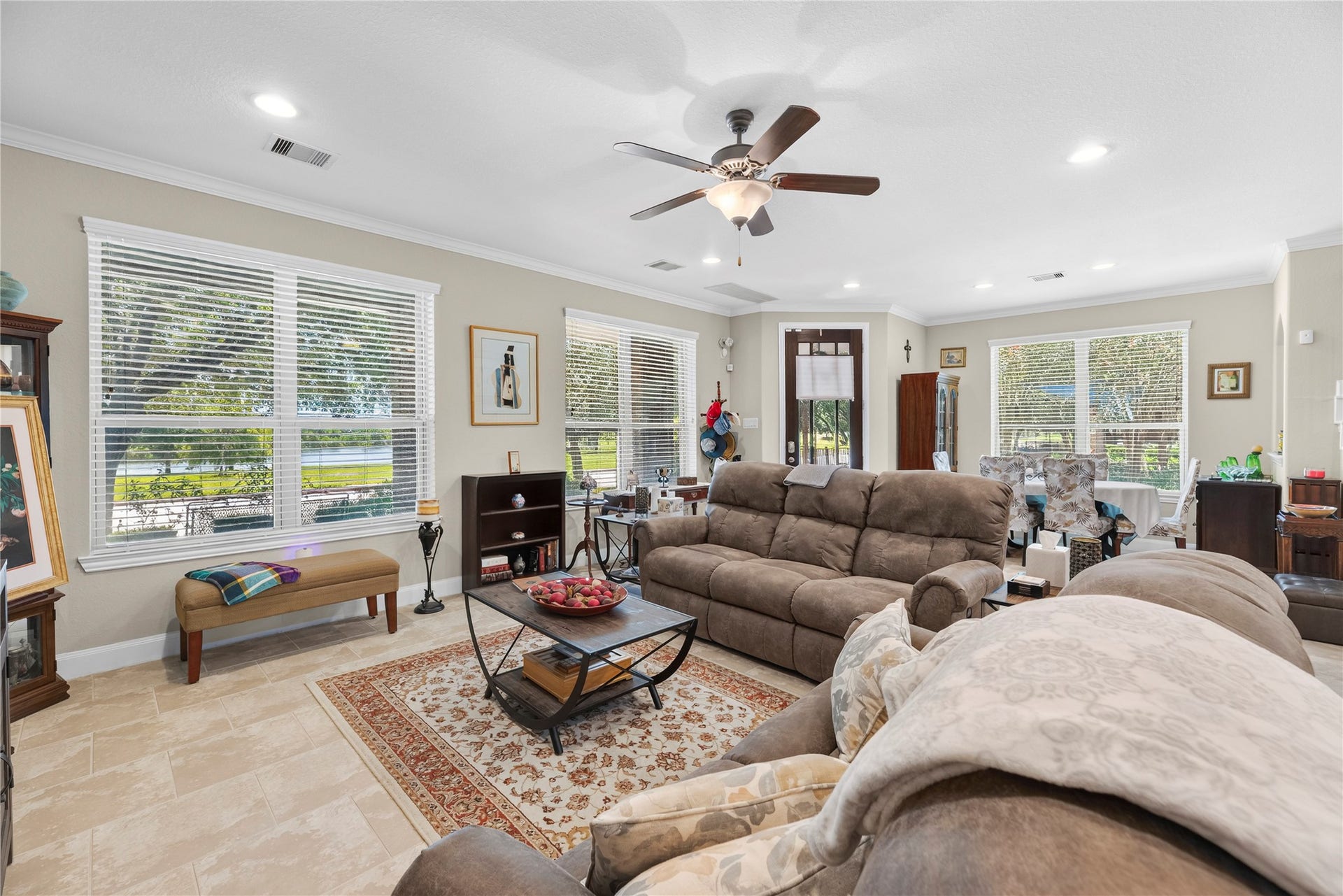 Spacious living room with recessed lights, crown molding, ceiling fan, tile floors, and an abundance of windows.