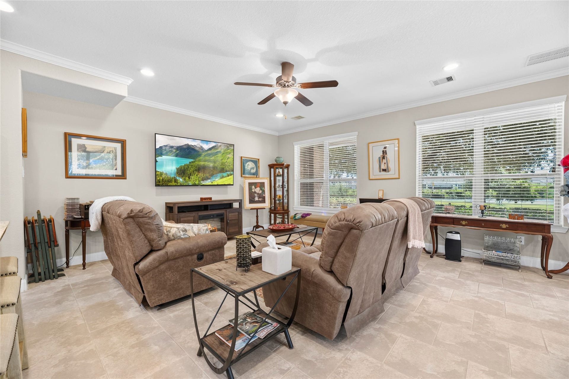 Spacious living room with recessed lights, crown molding, ceiling fan, tile floors, and an abundance of windows.