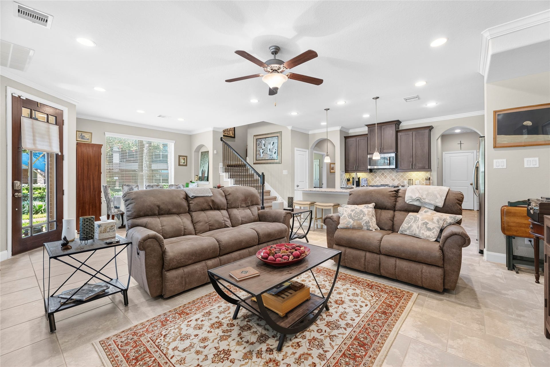 Spacious living room with recessed lights, crown molding, ceiling fan, tile floors, and an abundance of windows.