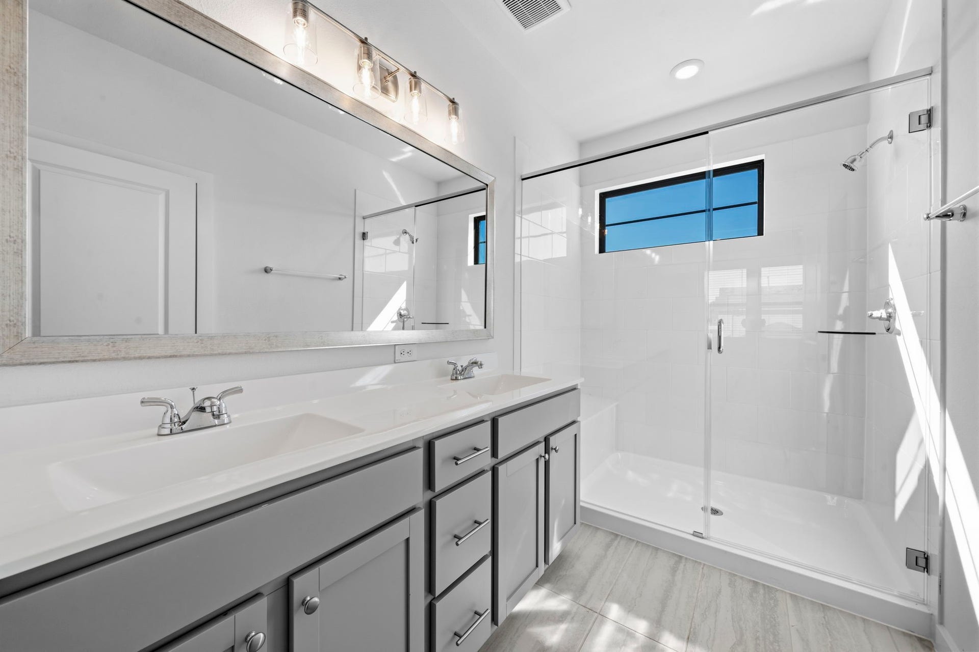 3317 City Heart Avenue, Richmond, TX 77406 Welcome to a bright and beautifully finished primary bathroom, featuring a spacious walk-in glass shower, double vanity, sleek grey cabinetry, and modern finishes. Natural light pours in through the window, creating a fresh and inviting space to start and end your day.