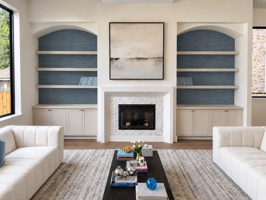 Custom build ins in the living room lined with grasscloth wallpaper, custom plastered mantle and marble surround