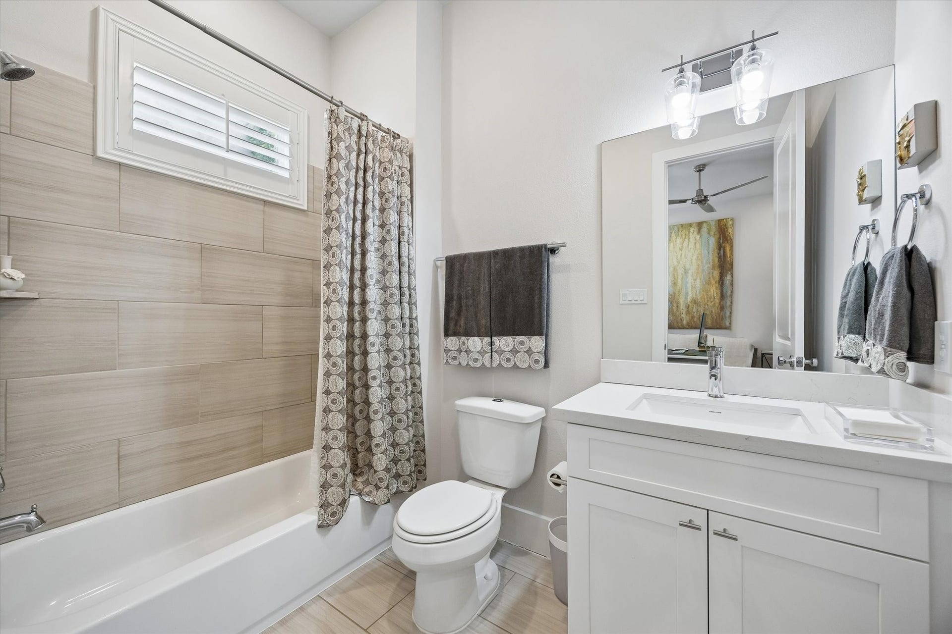 1226 W 21st Street, Houston, TX 77008 The guest ensuite bathroom is crisp and inviting with a clean white vanity, designer lighting, a tub and shower combo with tile surround, and a shuttered window that adds charm and natural light.