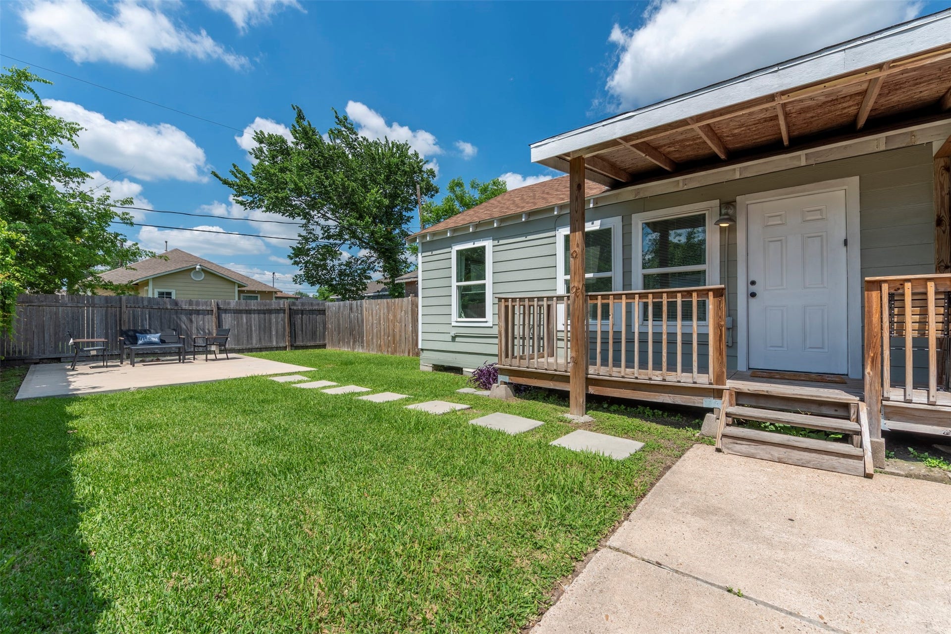 1121 Panama Street, #B, Houston, TX 77009 Exterior view featuring fresh sage-green lap siding, white trim, oversized single-pane windows, covered wood-porch with pendant light, concrete stepping stone path, and fully fenced yard.
