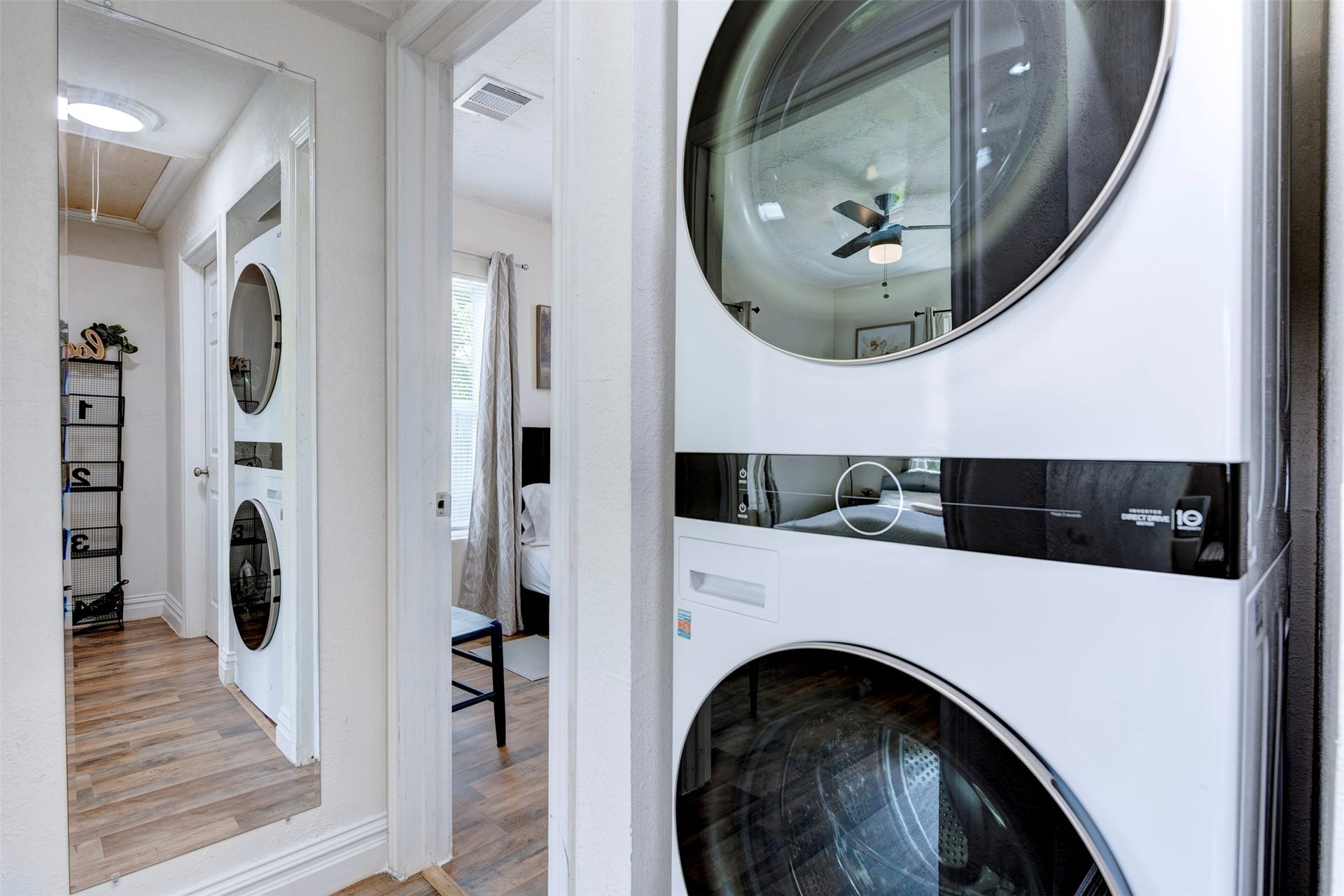 1121 Panama Street, #B, Houston, TX 77009 In-unit LG stacked front-load washer and dryer tucked into the hallway, with full-length mirror, wood-look flooring, and sightline directly into the bedroom.
