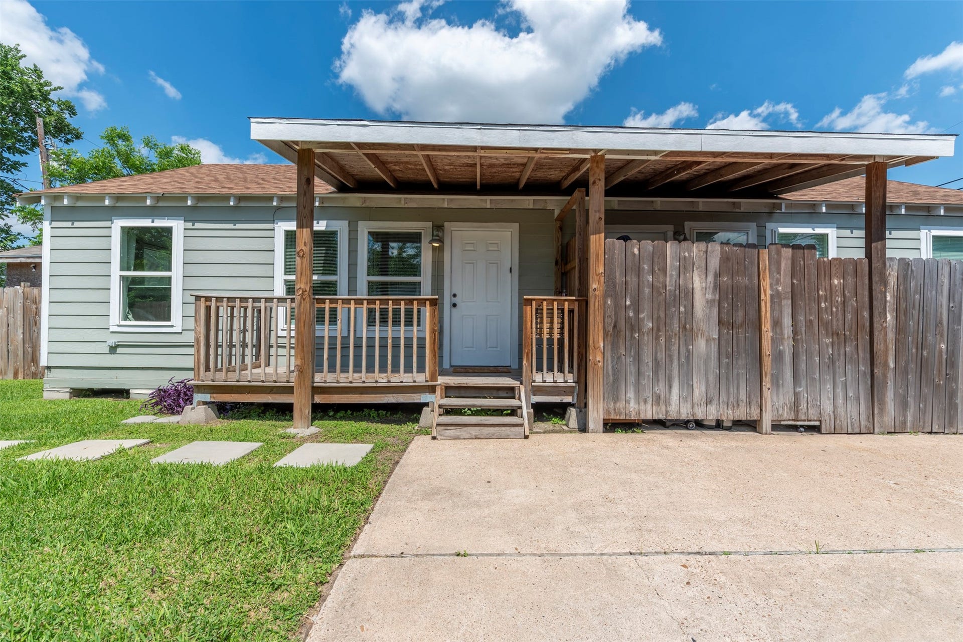 1121 Panama Street, #B, Houston, TX 77009 Front exterior with sage-green lap siding, white trim, covered front porch with exposed wood beam ceiling, wood railing, pendant wall light, and concrete driveway.