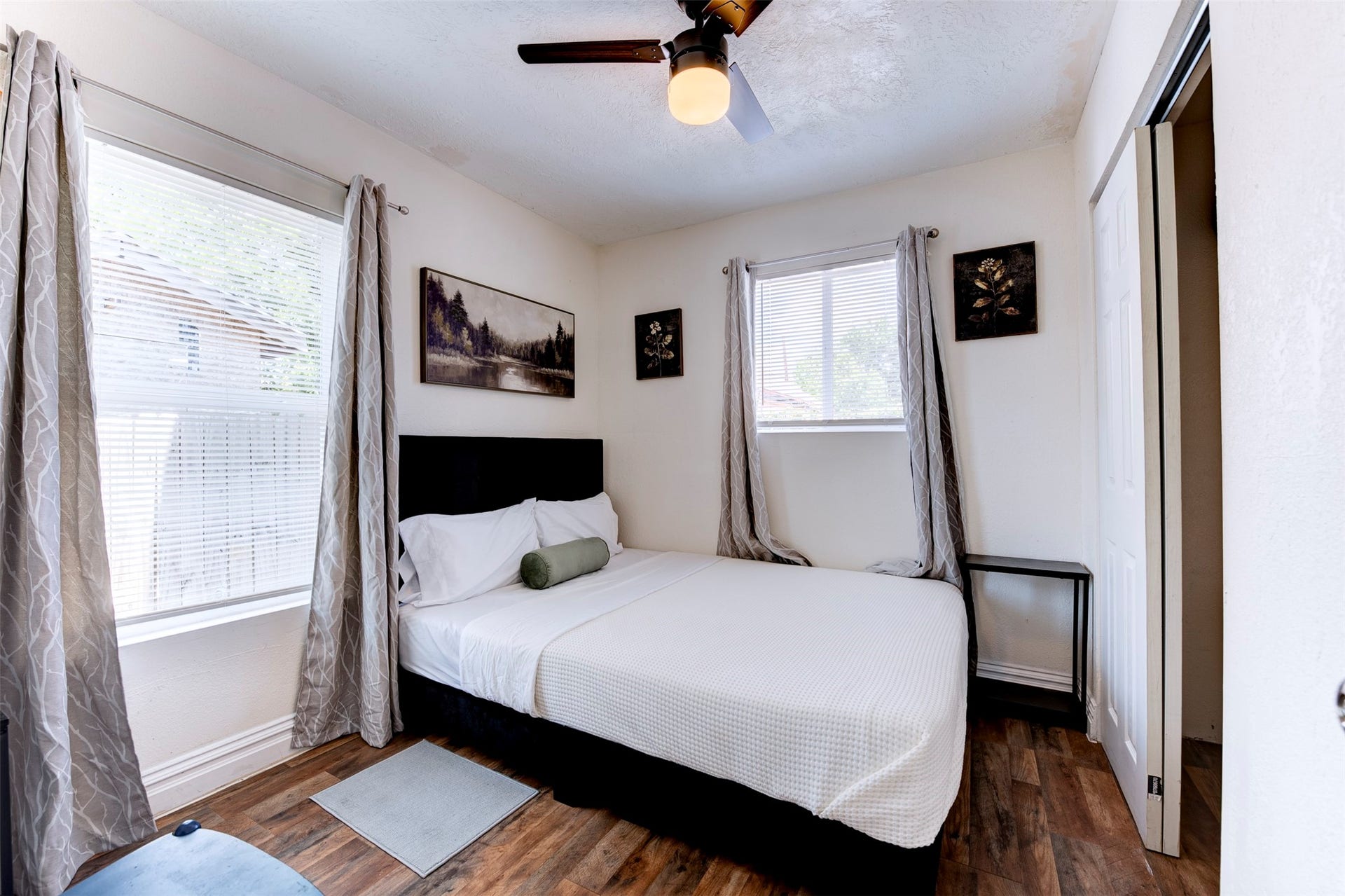 1121 Panama Street, #B, Houston, TX 77009 Bedroom featuring dark wood-look LVP flooring, ceiling fan with light kit, dual windows with blinds and grommet curtains, and a reach-in closet with sliding door.