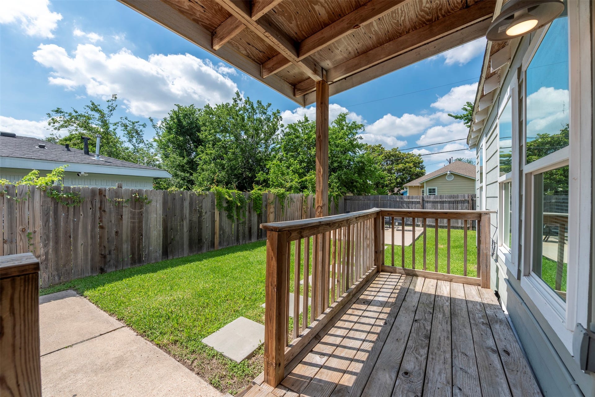 1121 Panama Street, #B, Houston, TX 77009 Covered front porch with exposed wood detail, pendant wall light, wood plank decking, wood baluster railing, and oversized single-pane window with direct sightlines to the fully fenced backyard.