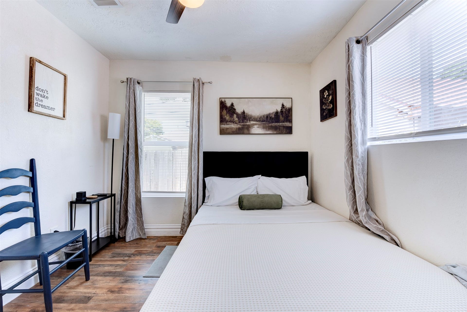 1121 Panama Street, #B, Houston, TX 77009 Alternate bedroom angle showing dual windows with natural light, dark wood-look LVP flooring, ceiling fan, and grommet curtain panels on black rod hardware.