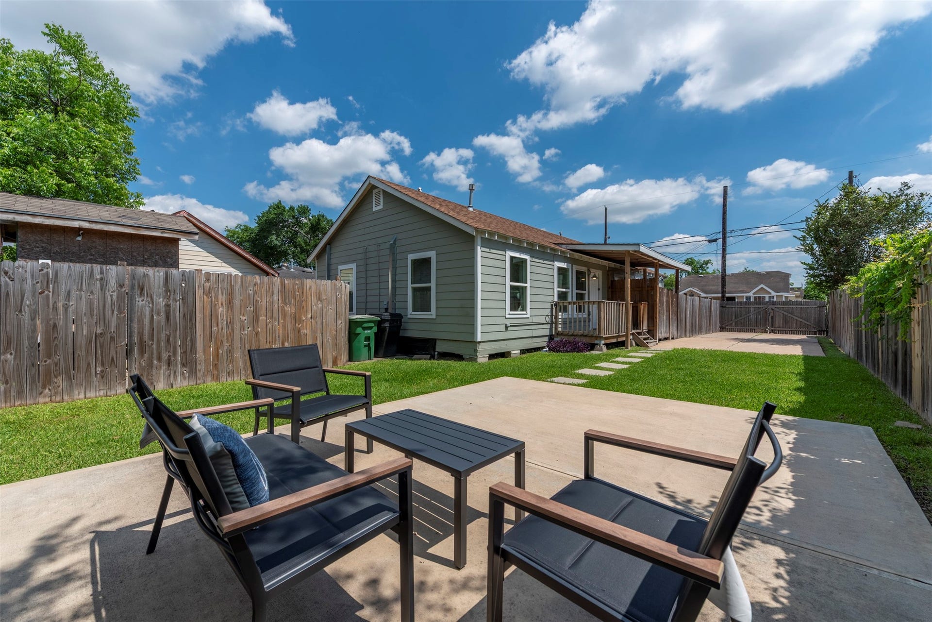 1121 Panama Street, #B, Houston, TX 77009 Backyard entertaining area with poured concrete patio, modern outdoor seating, manicured lawn, concrete stepping stone path, and covered back porch with wood beam detailing.