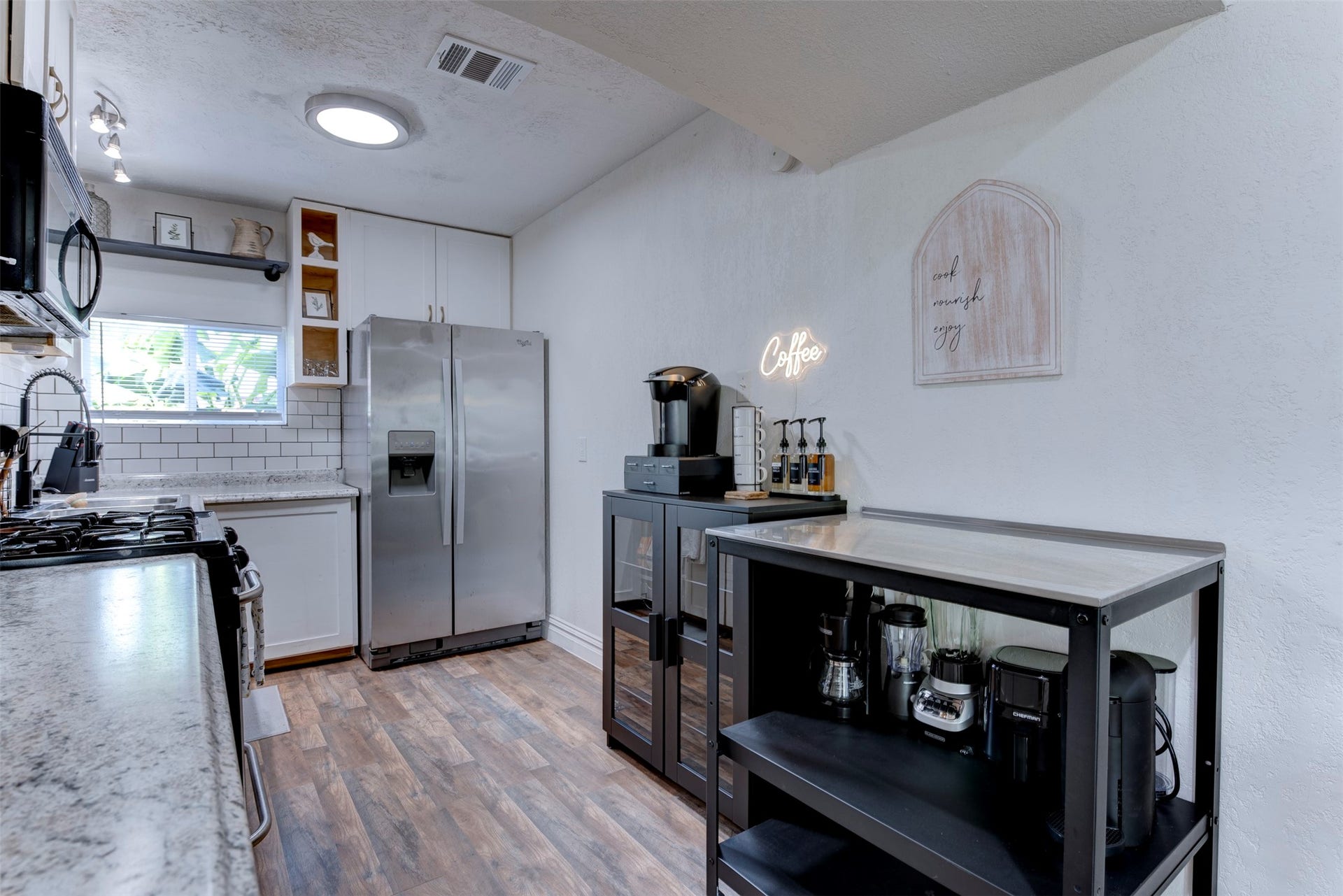 1121 Panama Street, #B, Houston, TX 77009 Kitchen wide view with GE gas range, granite countertops, Whirlpool stainless side-by-side refrigerator with ice and water dispenser, white subway tile backsplash, white shaker upper cabinetry, open pine cubbies, matte black pull-down faucet, track lighting, flush mount ceiling light, and dedicated black metal coffee and appliance station with Keurig brewer and syrup dispensers.