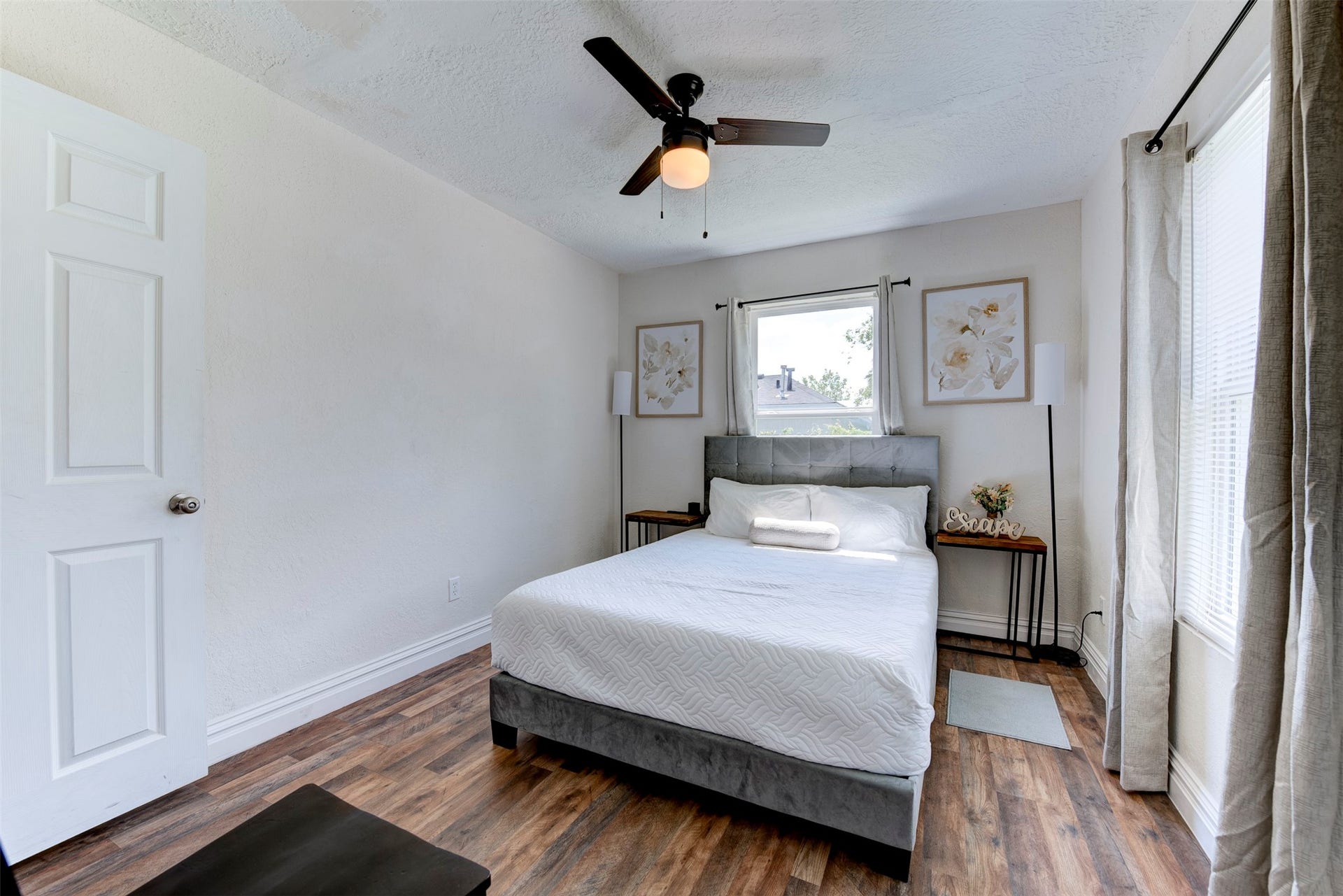1121 Panama Street, #B, Houston, TX 77009 Second bedroom with dark wood-look LVP flooring, ceiling fan with light kit, oversized window with grommet curtains on black rod, and six-panel interior door.