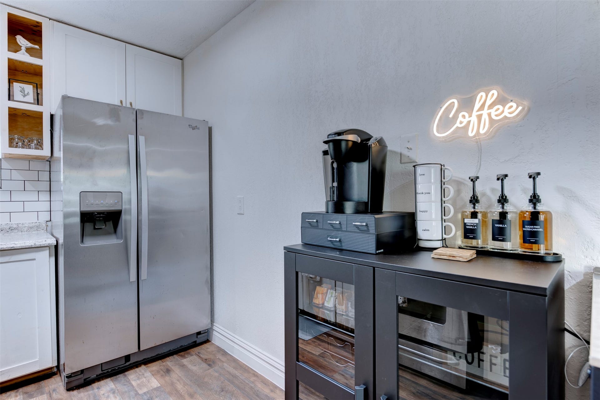 1121 Panama Street, #B, Houston, TX 77009 Coffee and appliance station with Keurig brewer, labeled syrup dispensers, white shaker cabinetry, and open pine cubby shelving