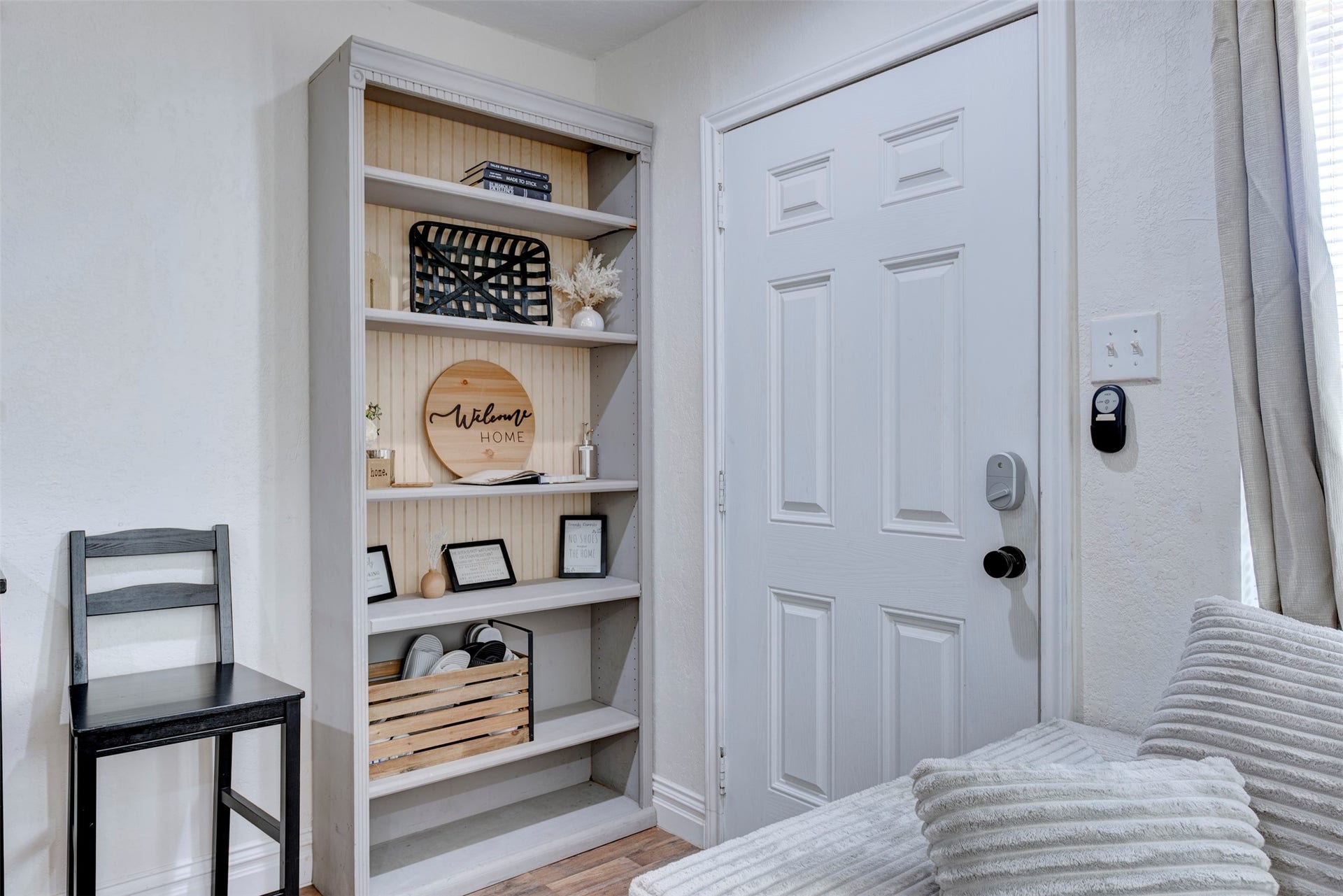 1121 Panama Street, #B, Houston, TX 77009 Entryway featuring white six-panel door with smart lock and black lever hardware, built-in five-shelf bookcase with natural pine beadboard back panel, wood-look LVP flooring, and oversized window with natural light.