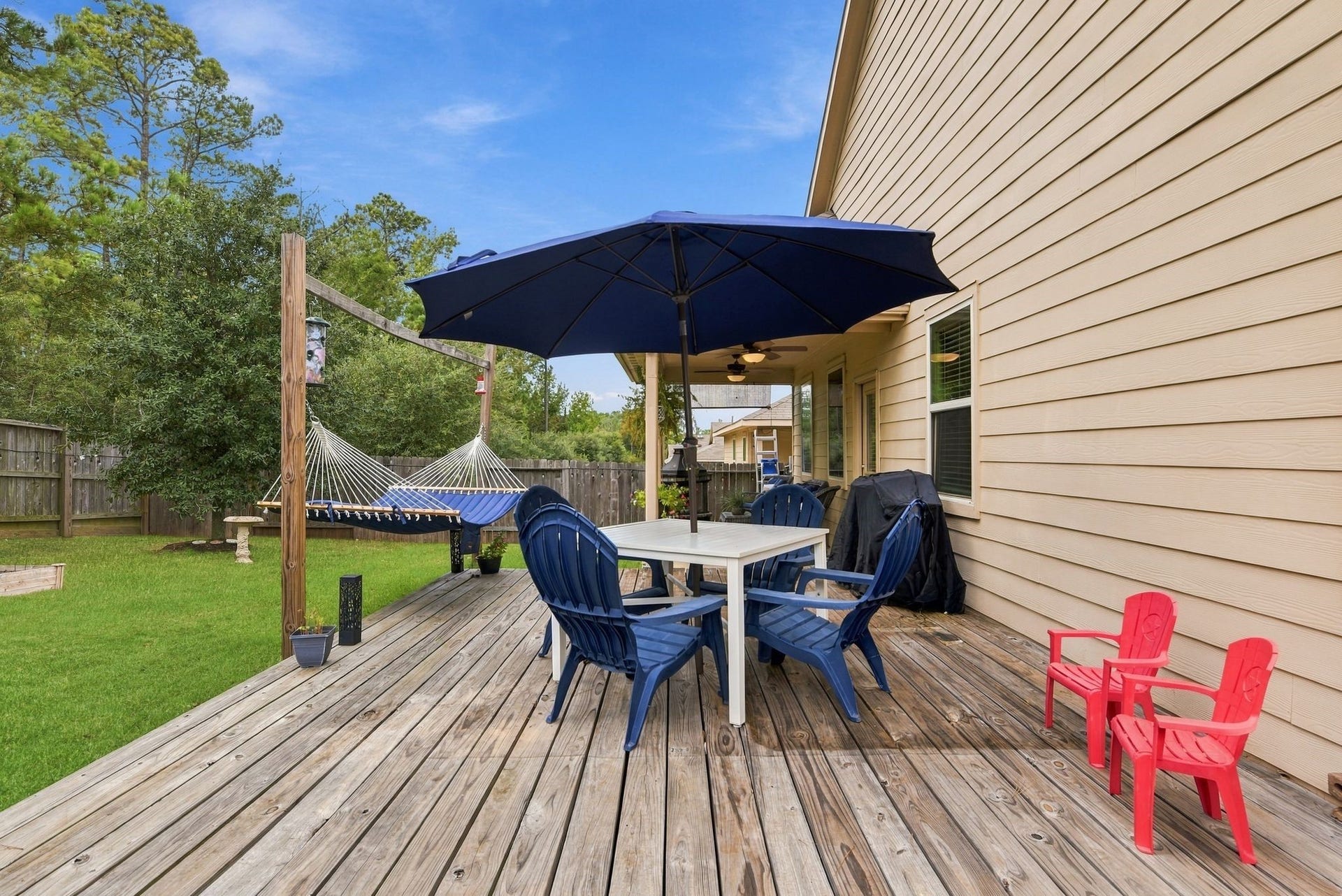 11371 Dawn Beach Lane, Conroe, TX 77304 Charming backyard deck featuring a cozy dining area under a large umbrella, perfect for outdoor entertaining, with a relaxing hammock and lush green lawn.