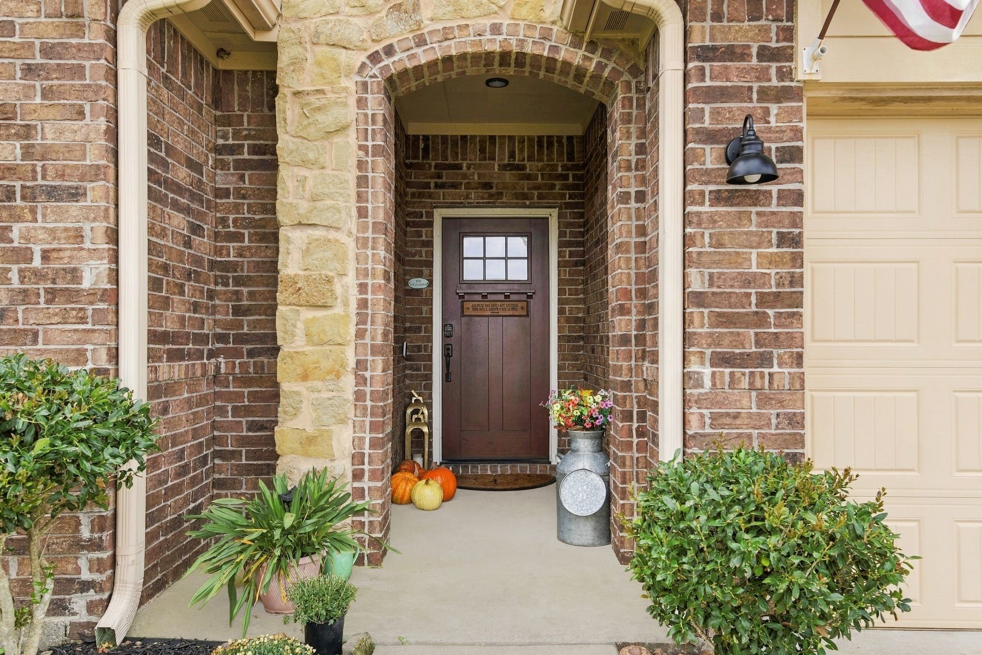 11371 Dawn Beach Lane, Conroe, TX 77304 Charming brick entryway with a rustic wooden door, adorned with seasonal decor and surrounded by lush greenery, creating an inviting welcome.