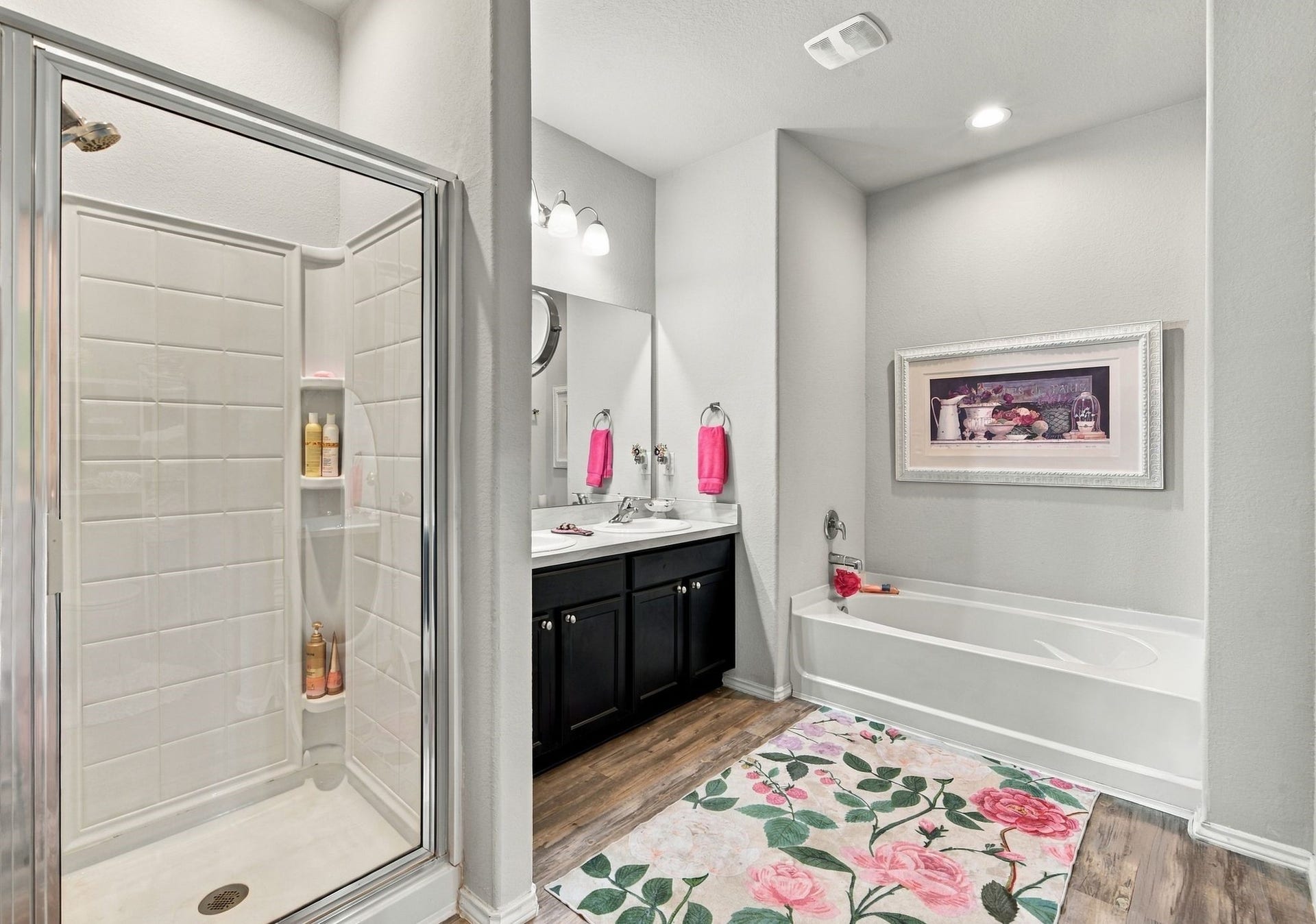 11371 Dawn Beach Lane, Conroe, TX 77304 Elegant bathroom featuring a glass-enclosed shower, a stylish vanity with dual sinks, and a relaxing bathtub. The floral rug and artwork add a touch of charm.