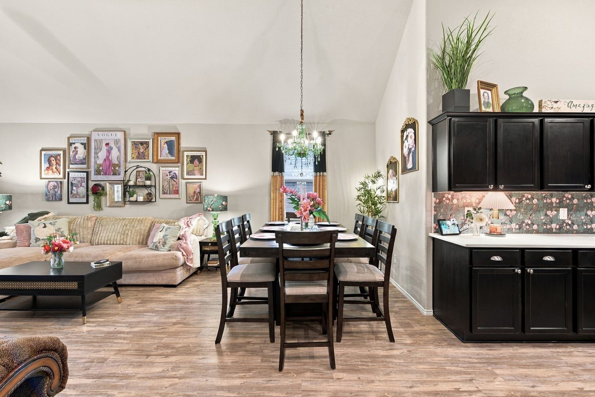11371 Dawn Beach Lane, Conroe, TX 77304 Charming open-concept living and dining area with stylish laminate flooring, elegant wall art, and a cozy sectional sofa. The dining space flows seamlessly into a kitchen featuring dark cabinetry and floral backsplash, creating a warm and inviting atmosphere.