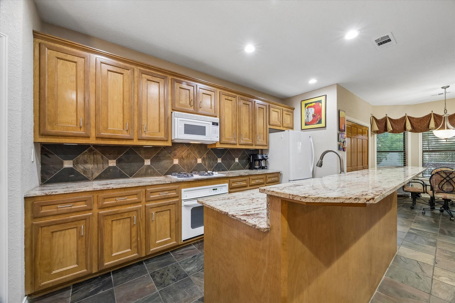 3040 Bayshore Drive, Bacliff, TX 77518 Kitchen featuring extensive cabinetry, granite countertops, and tile backsplash. Functional layout with ample prep space, built-in appliances, and center island for additional workspace.