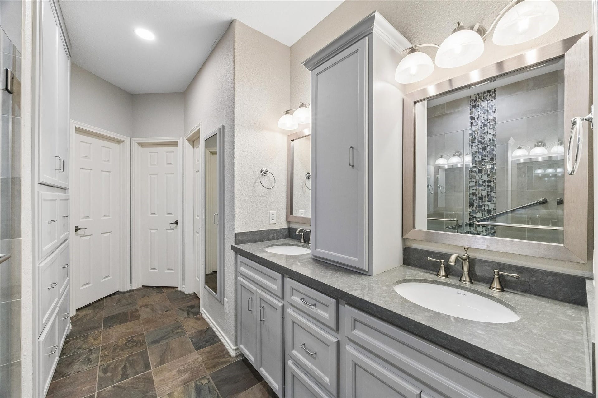 3040 Bayshore Drive, Bacliff, TX 77518 Primary bathroom with dual vanities, updated cabinetry, and ample storage. Walk-in shower with tile surround and glass enclosure provides a clean, modern finish. Two walk-in closets and a bonus space currently called the "snore" room but can be used for multiple purposes.