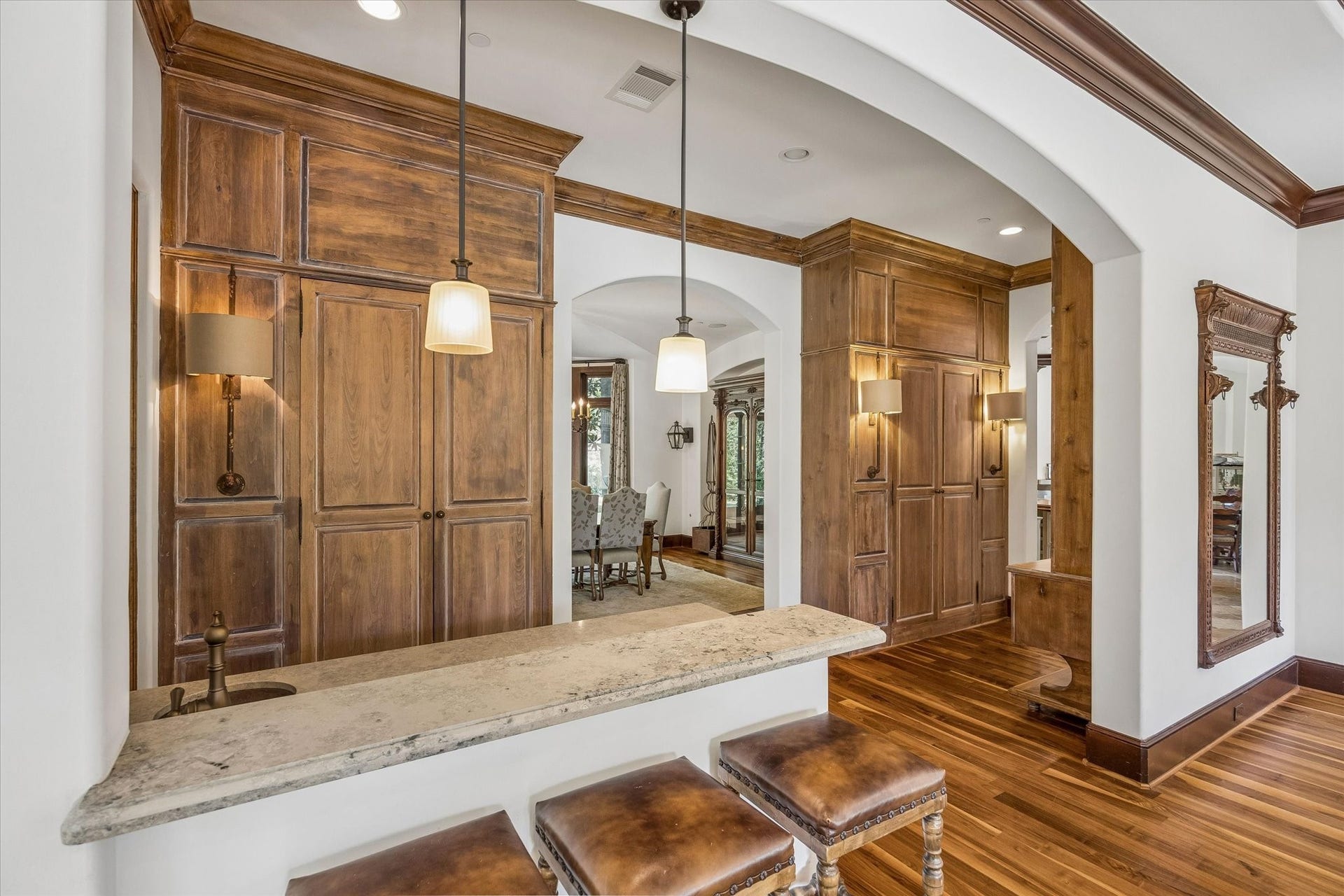 34 Liberty Bell Circle, Bunker Hill Village, TX 77024 A closer look at the wet bar reveals a generous stone countertop with seating, a built-in sink, and extensive custom wood cabinetry, conveniently positioned between the family and dining rooms.