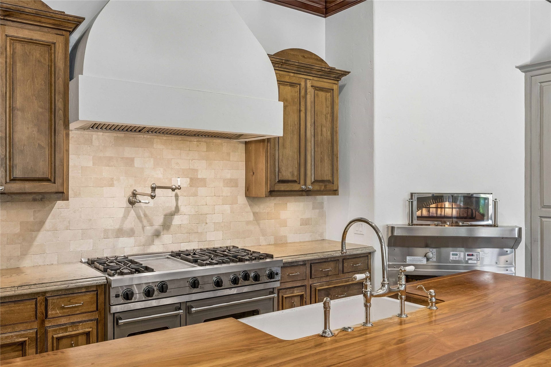 34 Liberty Bell Circle, Bunker Hill Village, TX 77024 A chefs kitchen featuring a Viking gas range, custom vent hood, pot filler, and stone backsplash, complemented by a generous wood-topped island with farmhouse sink.