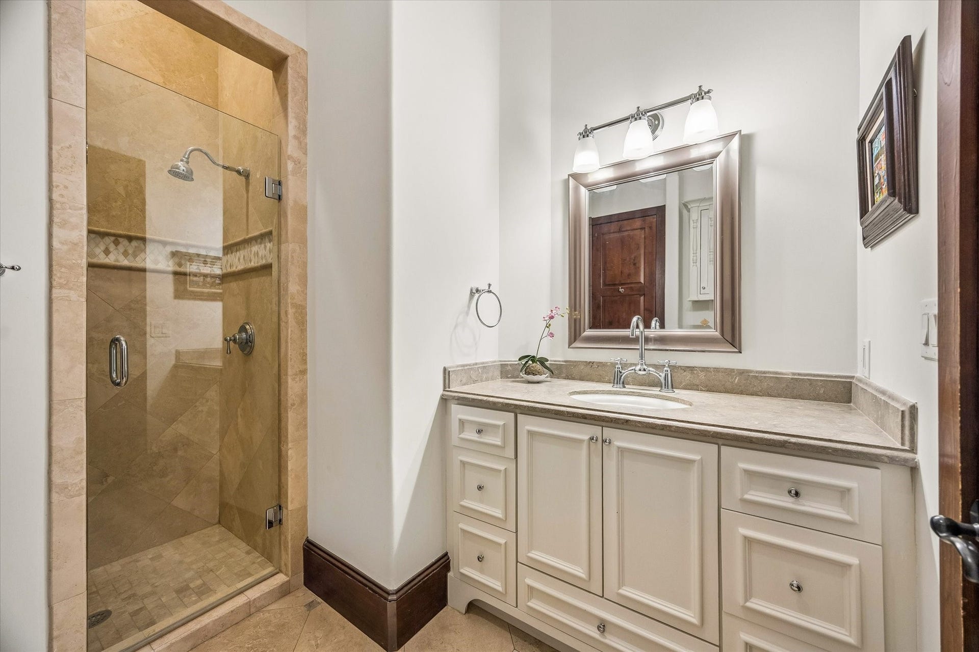 34 Liberty Bell Circle, Bunker Hill Village, TX 77024 The first-floor guest bath features a stone-topped vanity and a walk-in shower with frameless glass enclosure, natural stone tile, and decorative detailing.