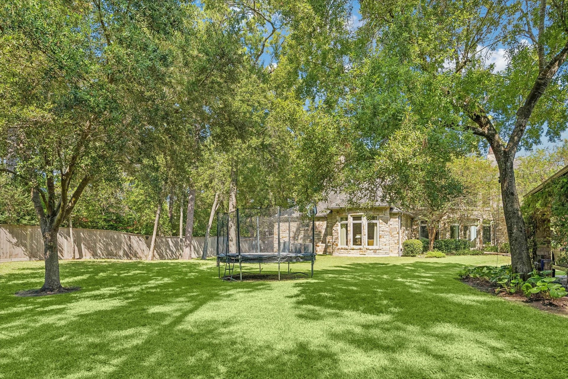 34 Liberty Bell Circle, Bunker Hill Village, TX 77024 A sprawling backyard offers an expansive lawn shaded by mature trees, creating a peaceful setting with plenty of room for outdoor activities, recreation, and gatherings. The generous green space provides a wonderful complement to the home's impressive outdoor living areas.
